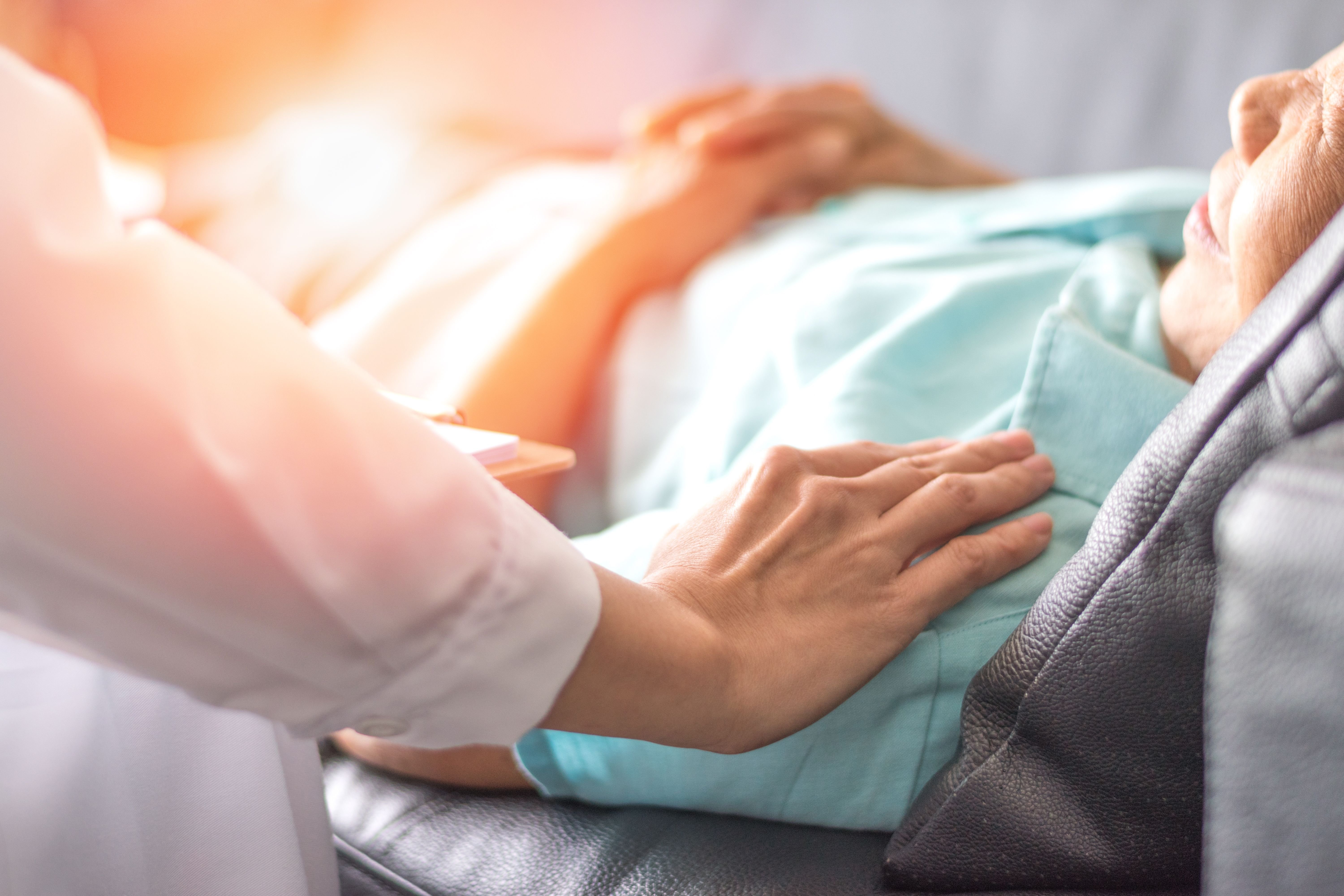 Paciente en cama de hospital y manos de acompañante. | Foto: Shutterstock