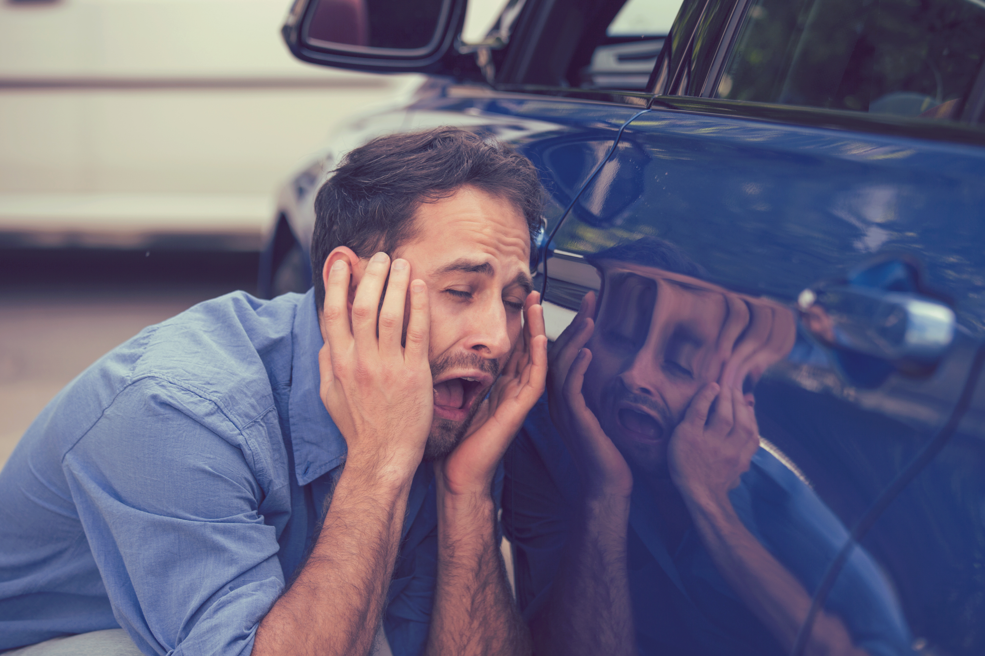 Joven frustrado y disgustado mirando los arañazos y abolladuras de su Automóvil al aire libre | Fuente: Getty Images
