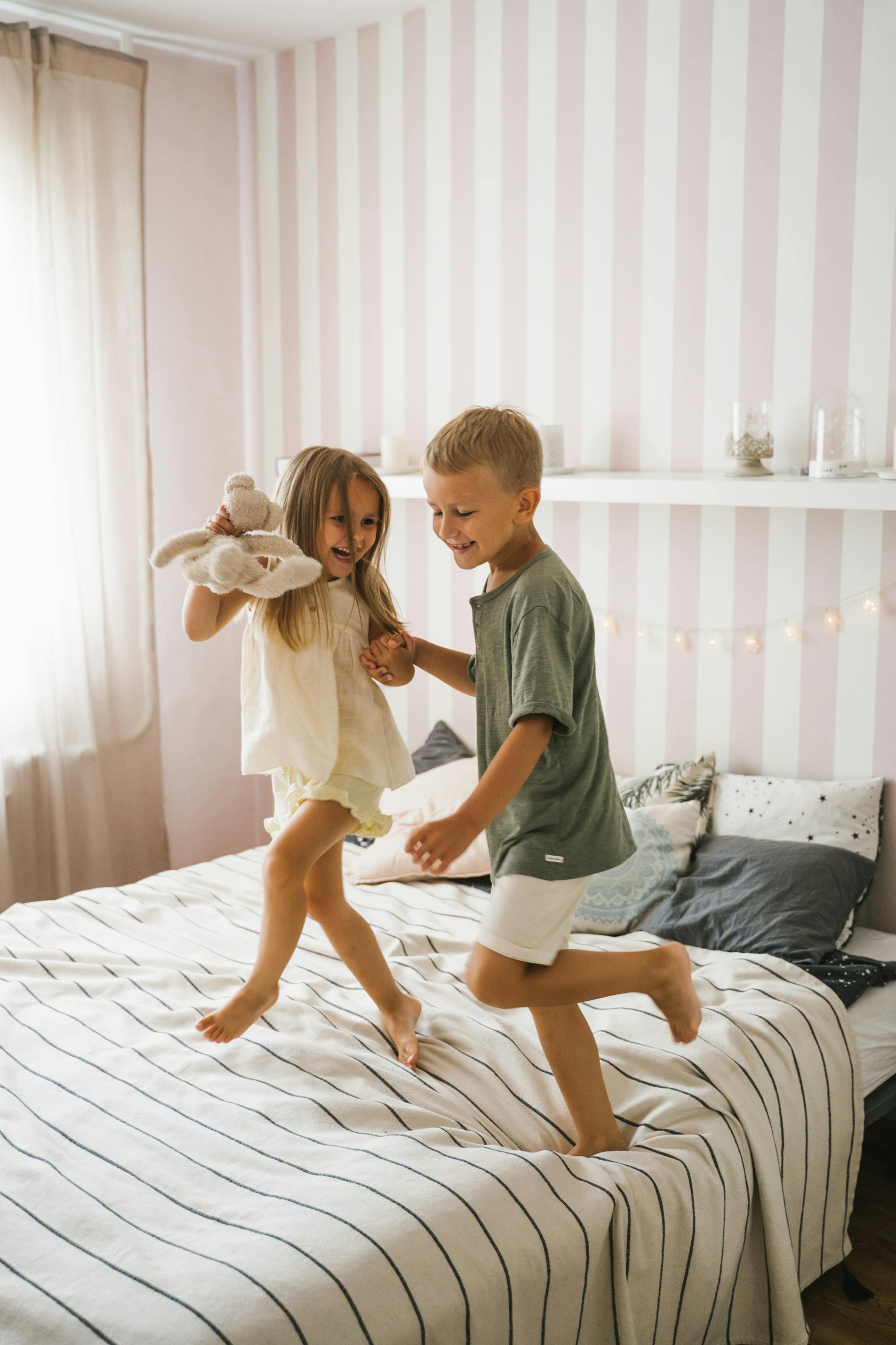 Un niño y una niña felices bailando en la cama | Foto: Pexels