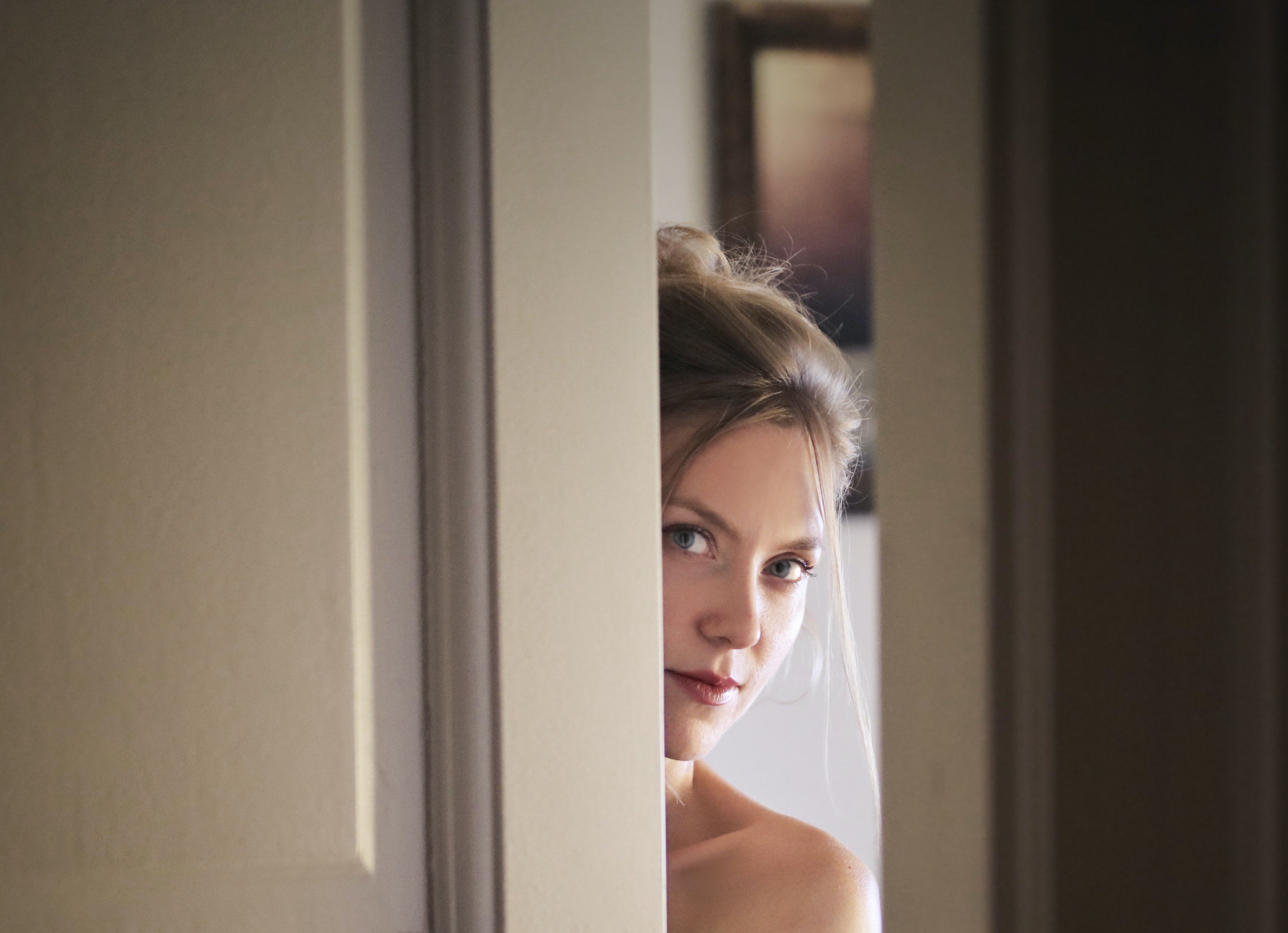 Una joven mujer se asoma a una puerta. | Foto: Pexels