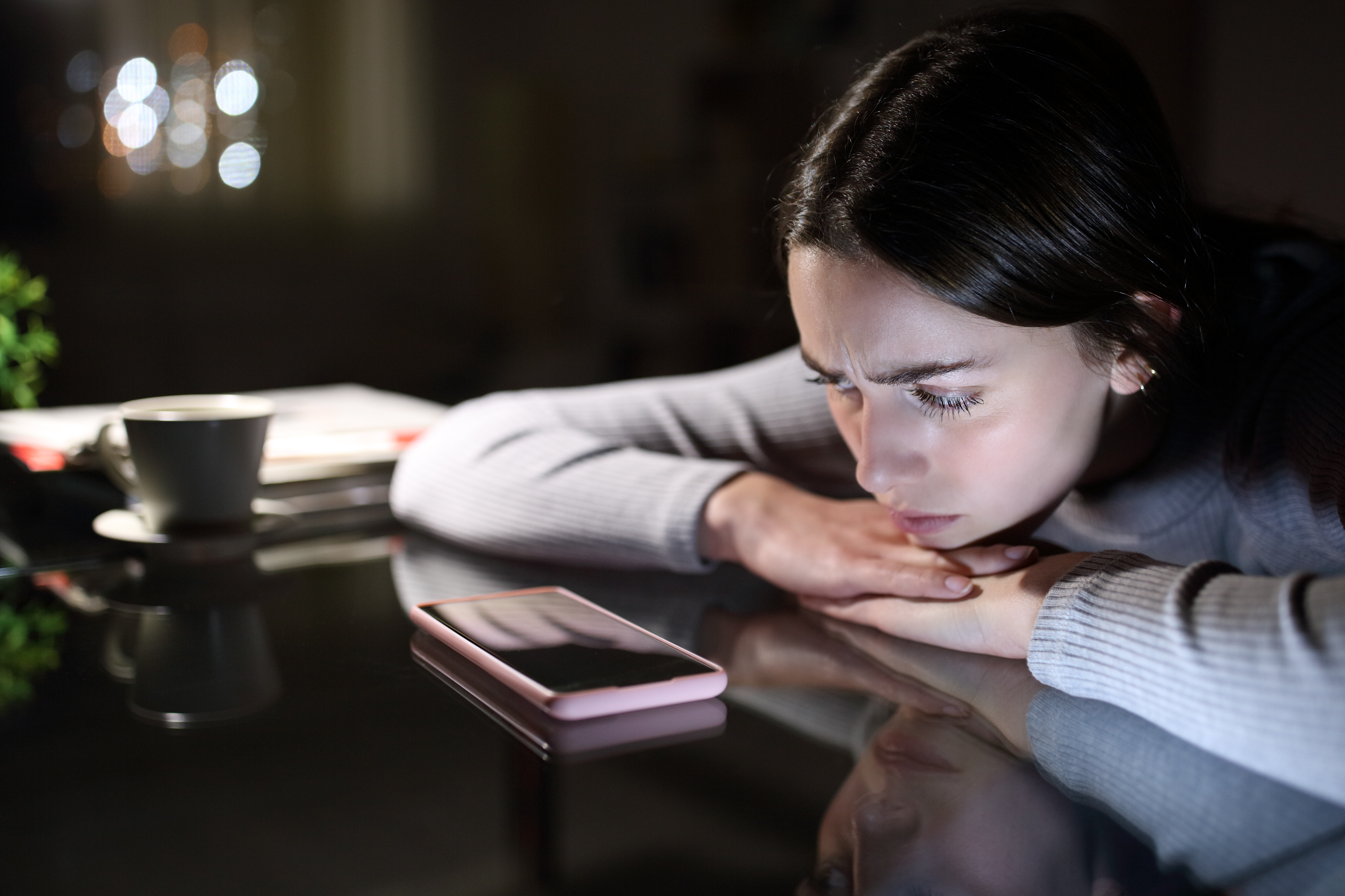 Mujer triste con un teléfono móvil por la noche en casa. | Fuente: Shutterstock