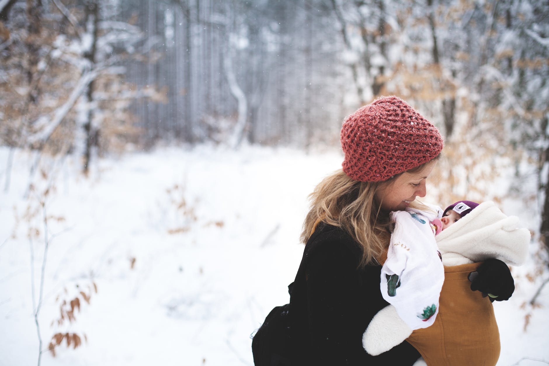 Mujer sosteniendo a su bebé en sus brazos en medio de un paisaje nevado. | Foto: Pexels