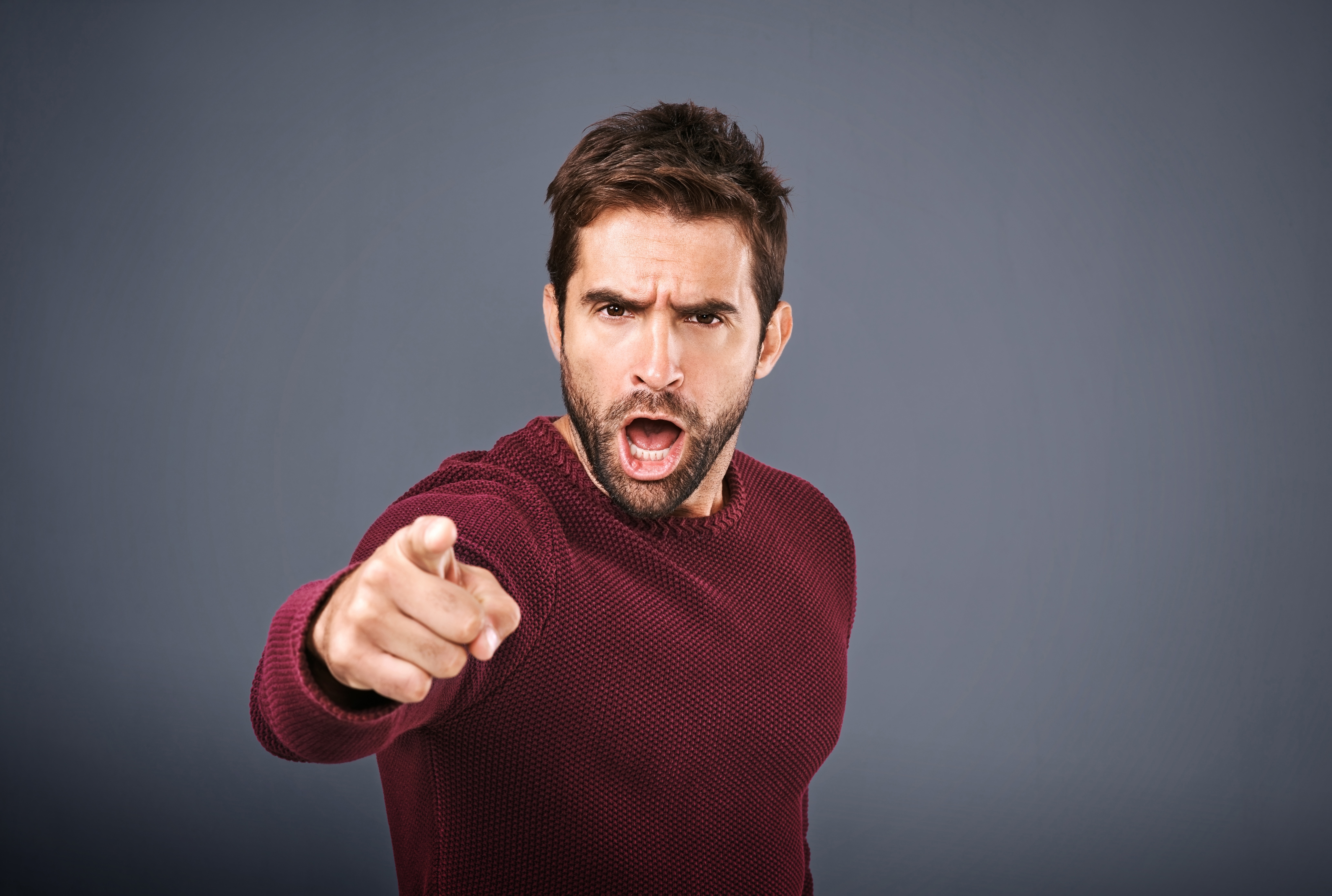 Instantánea de un hombre señalando con el dedo, enfadado, sobre un fondo gris. | Fuente: Shutterstock