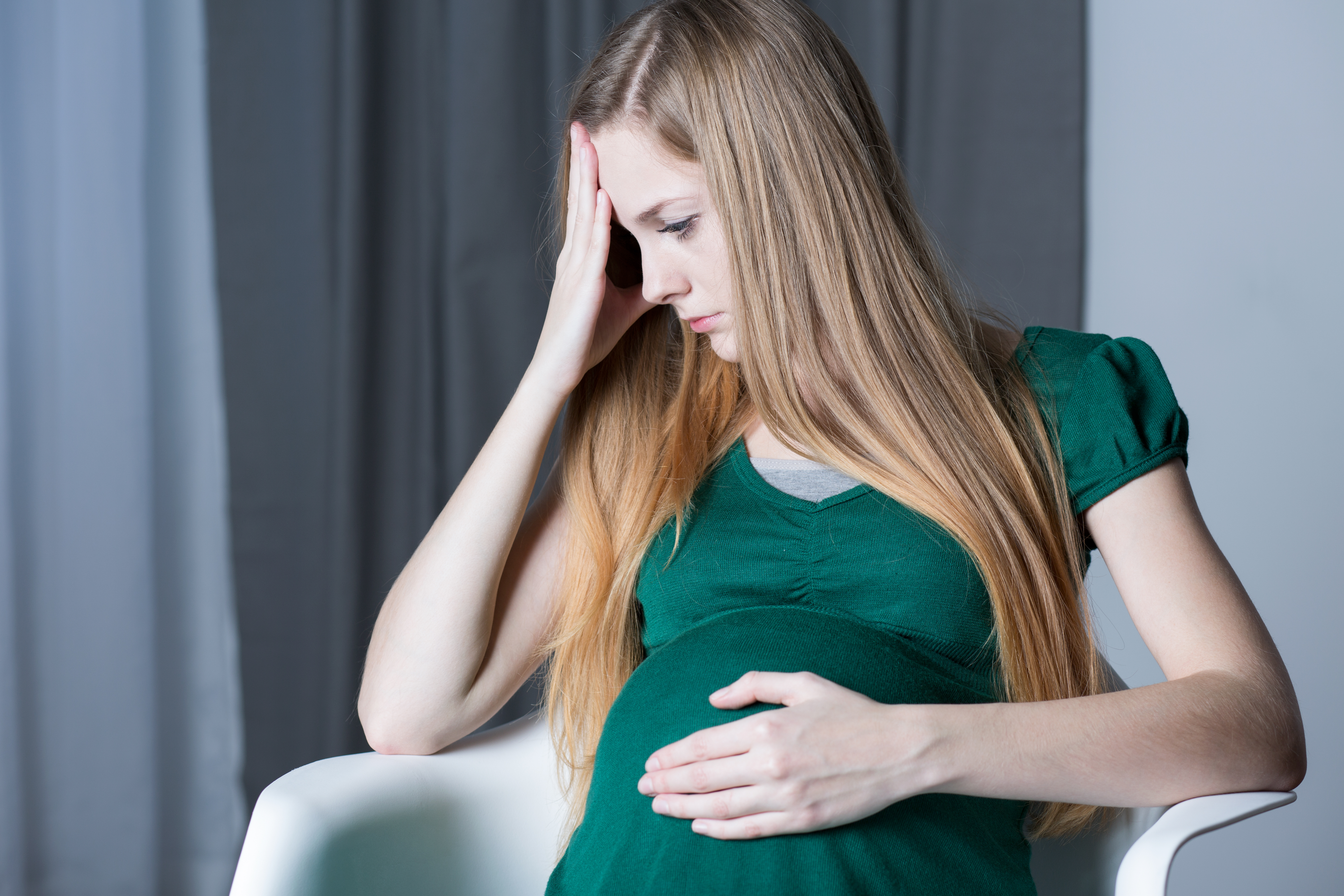 Adolescente triste en avanzado estado de gestación tocándose con una mano el vientre | Fuente: Shutterstock.com