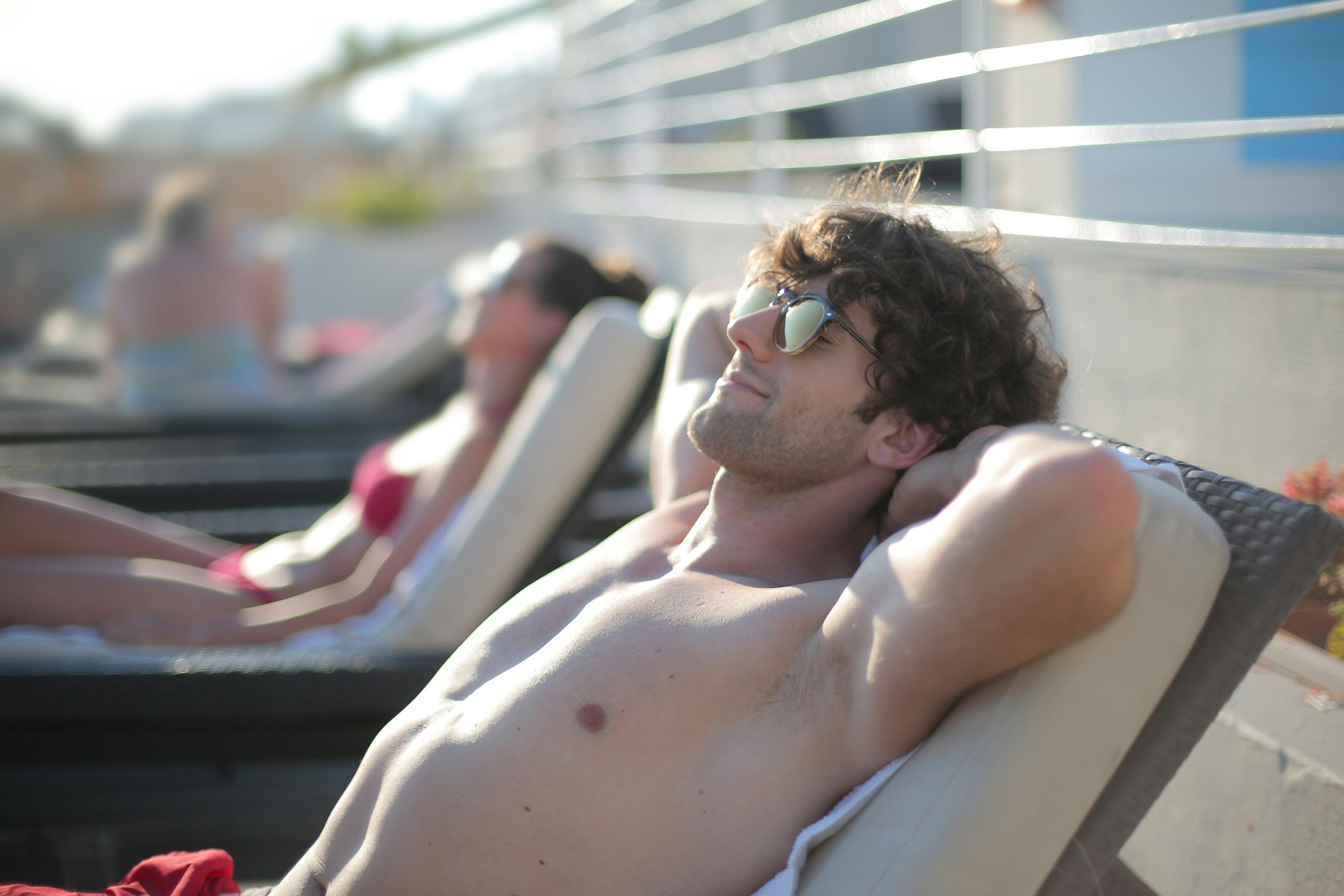 Un hombre feliz con gafas de sol tumbado en una tumbona | Fuente: Pexels