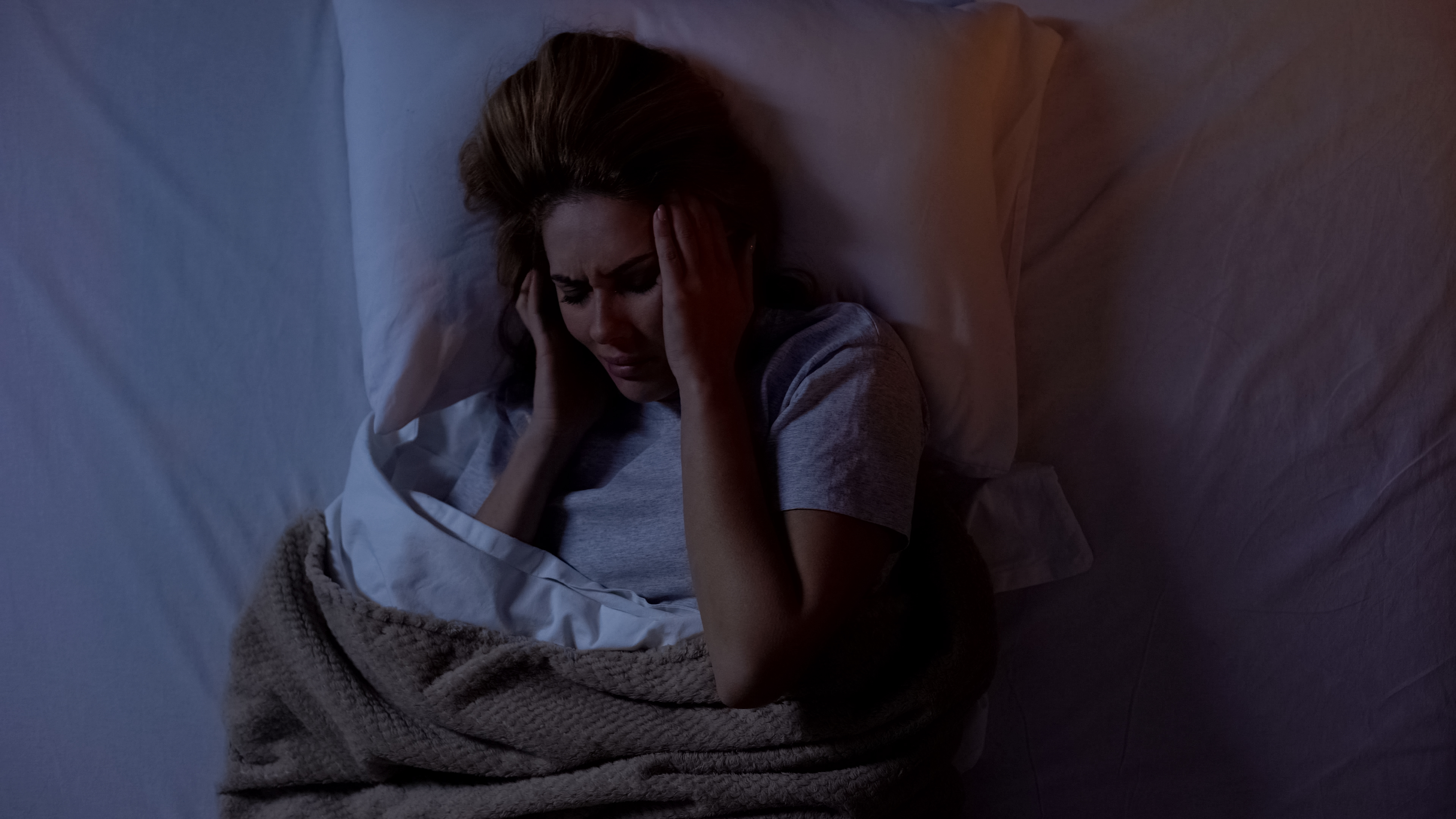 Mujer sujetándose la cabeza en la cama, sufriendo dolor de cabeza tras despertarse por la noche. | Fuente: Shutterstock