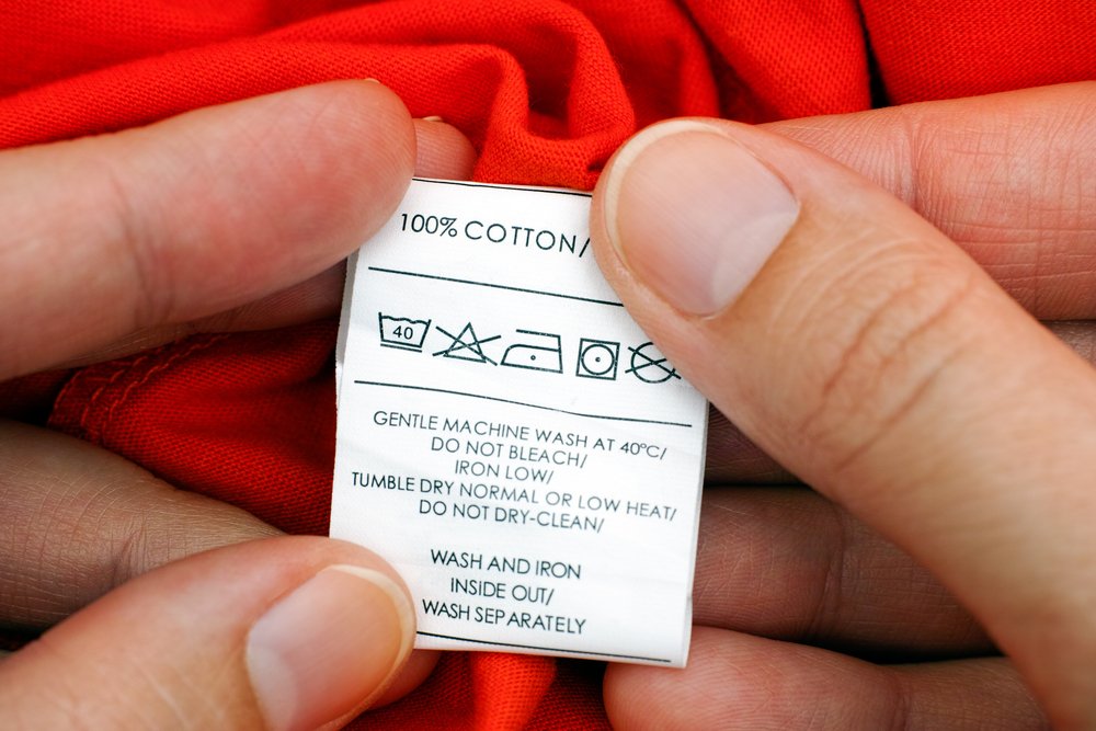 Manos de mujer sosteniendo la etiqueta con instrucciones de lavado. | Foto: Shutterstock