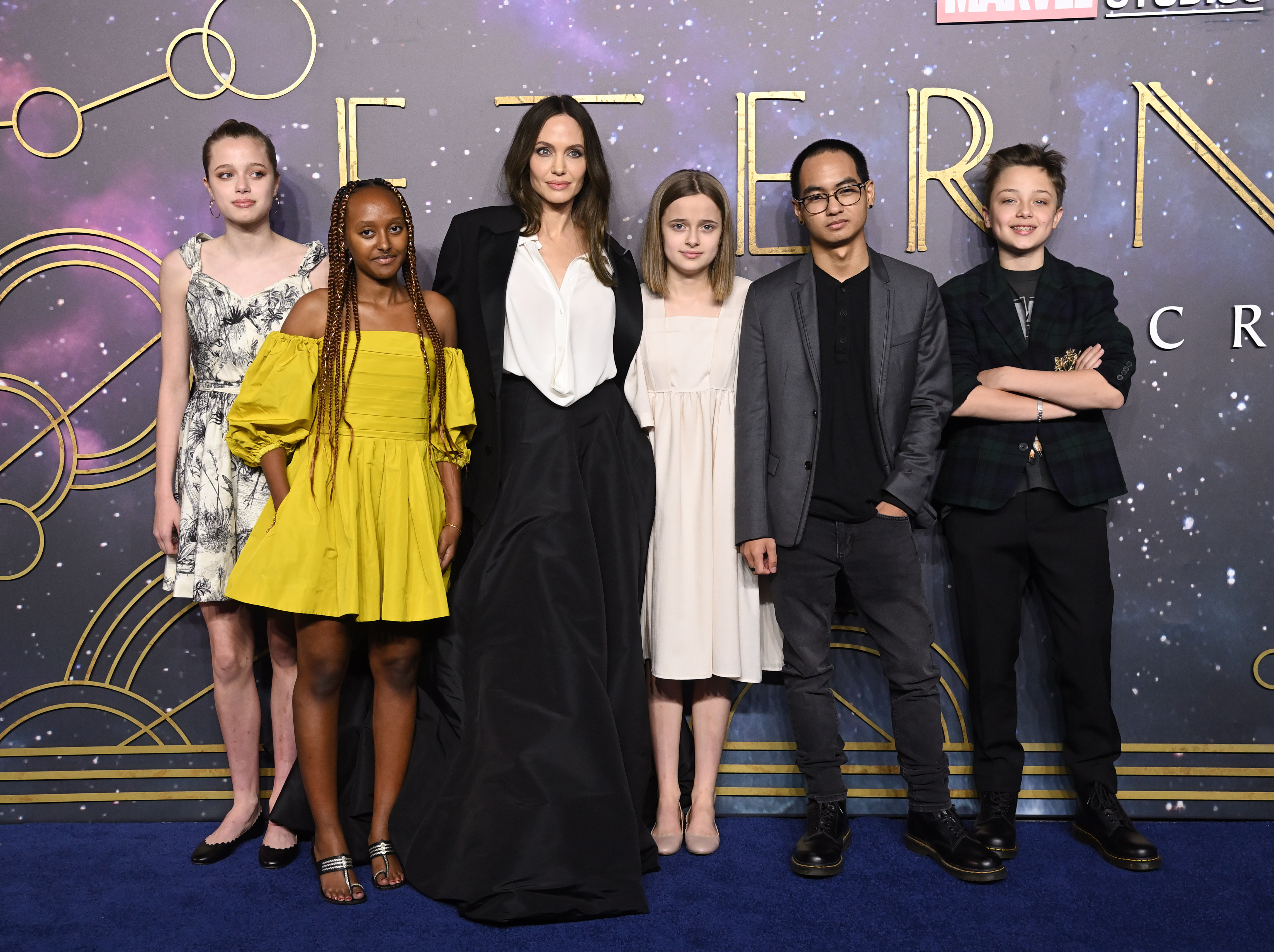 Angelina Jolie posa con sus seis hijos en el estreno europeo de Eternals, luciendo un vestido negro hasta el suelo sobre una blusa blanca, mientras sus hijos permanecen a su lado con una mezcla de atuendos formales e informales. La familia se reunió en la alfombra azul para el evento de 2021, años antes de la renovada atención en torno al uso del apellido Jolie por parte de los hijos. | Fuente: Getty Images