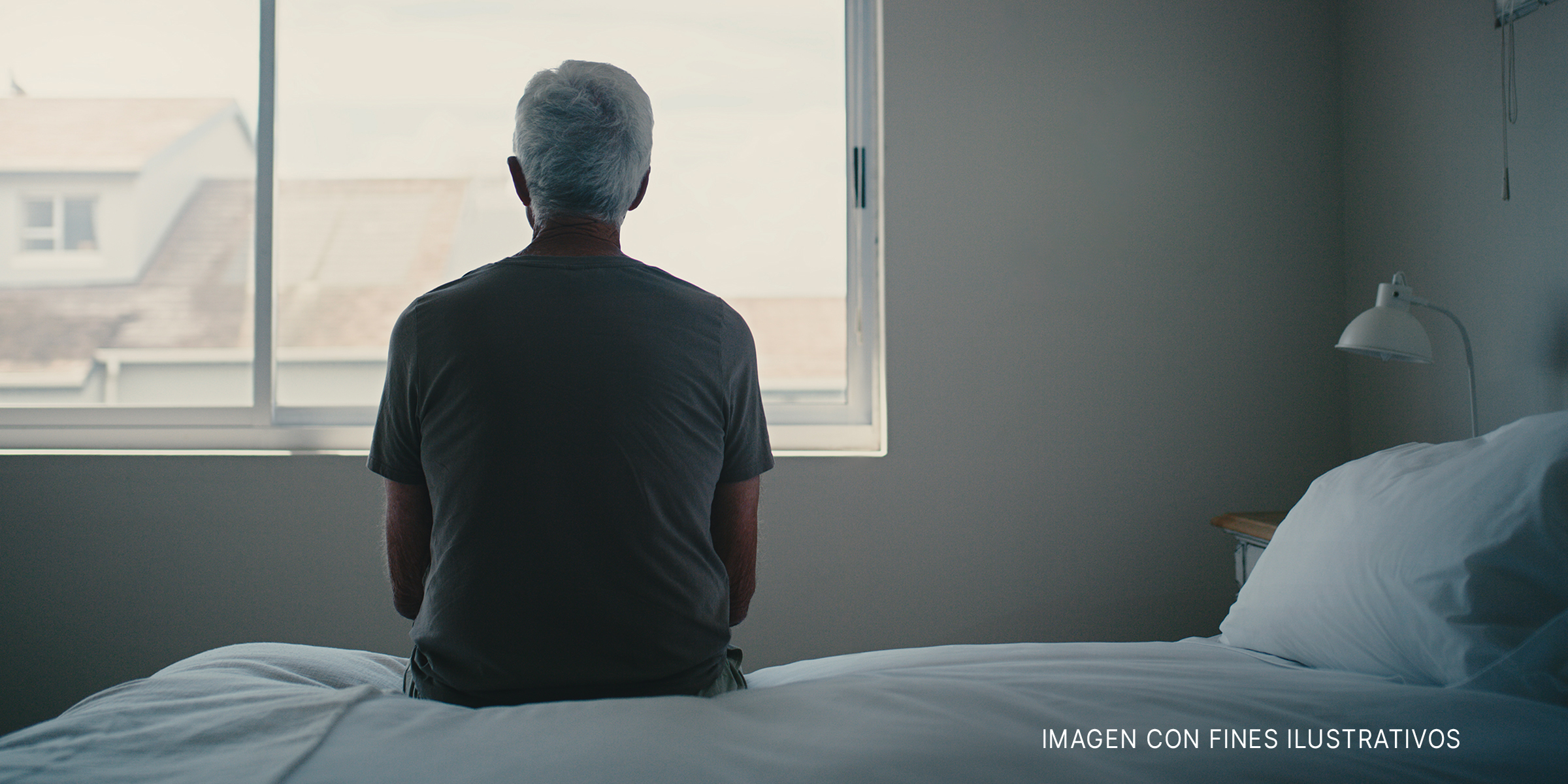 Un hombre sentado en una cama mirando por una ventana. | Foto: Shutterstock