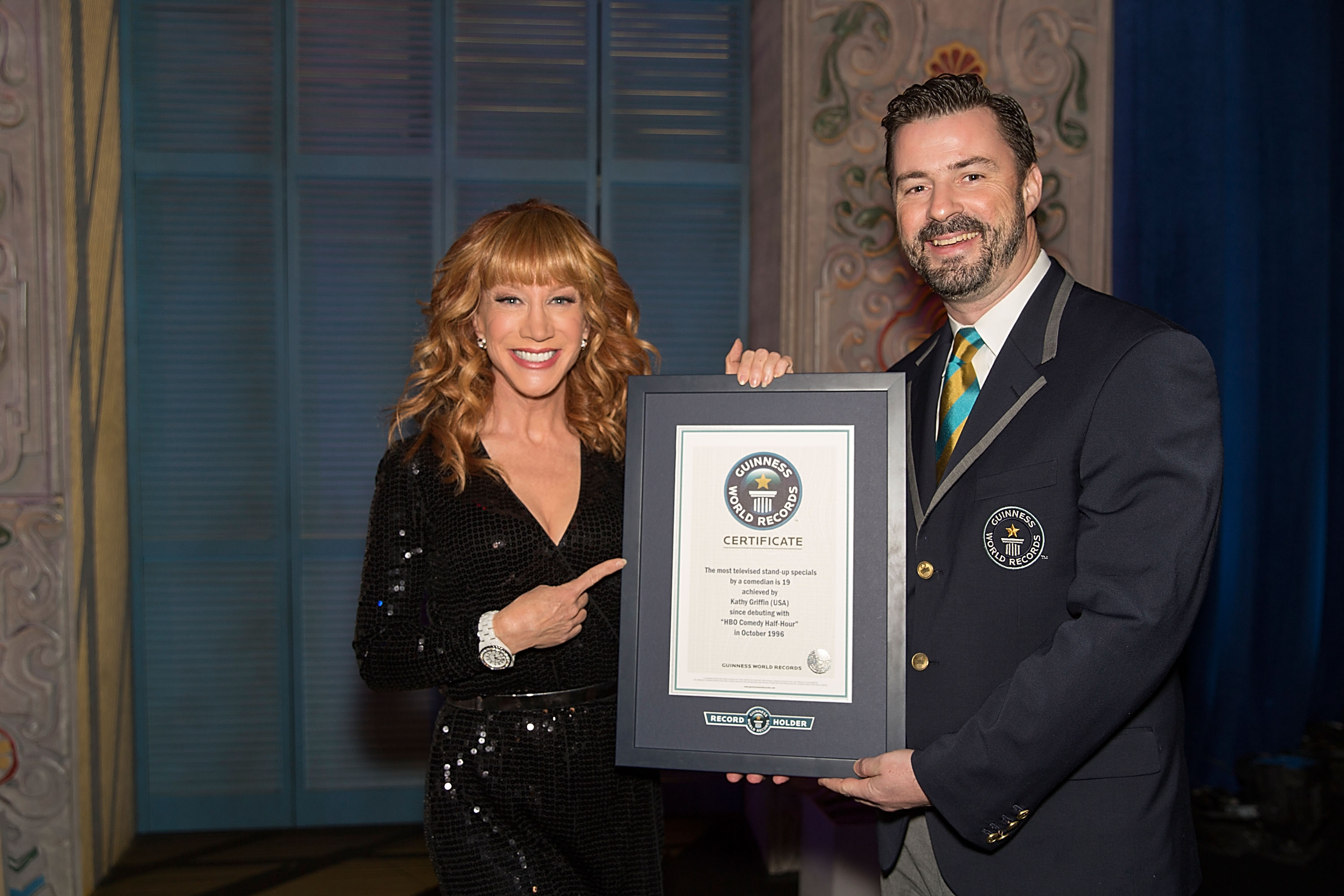 Kathy Griffin con un representante del Récord Guinness tras batir el Récord Guinness de mayor número de especiales de stand-up comedy por un cómico el 24 de noviembre de 2013 | Fuente: Getty Images