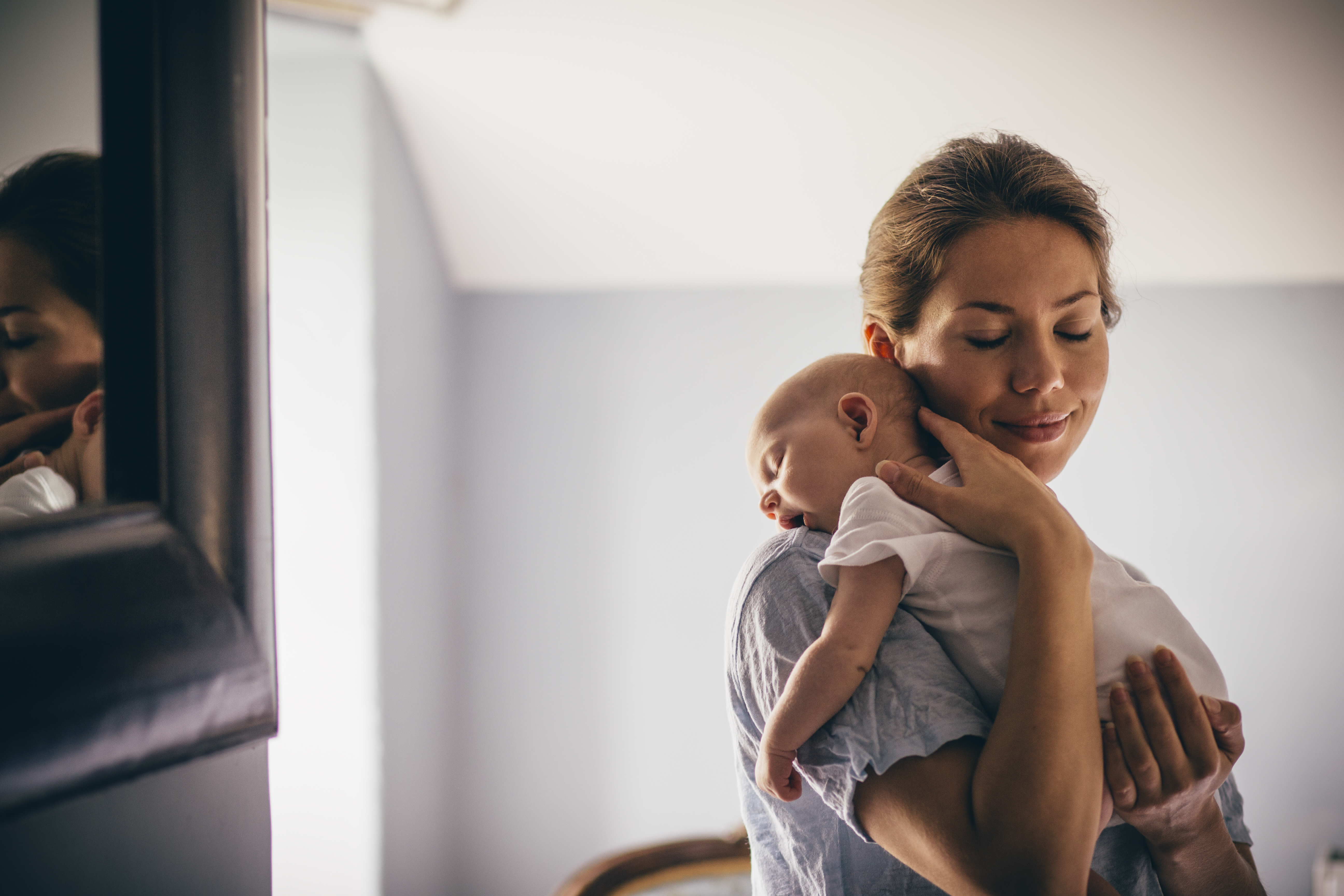 Una madre joven y feliz sonríe mientras acuna a su bebé dormido en brazos. | Foto: Getty Images