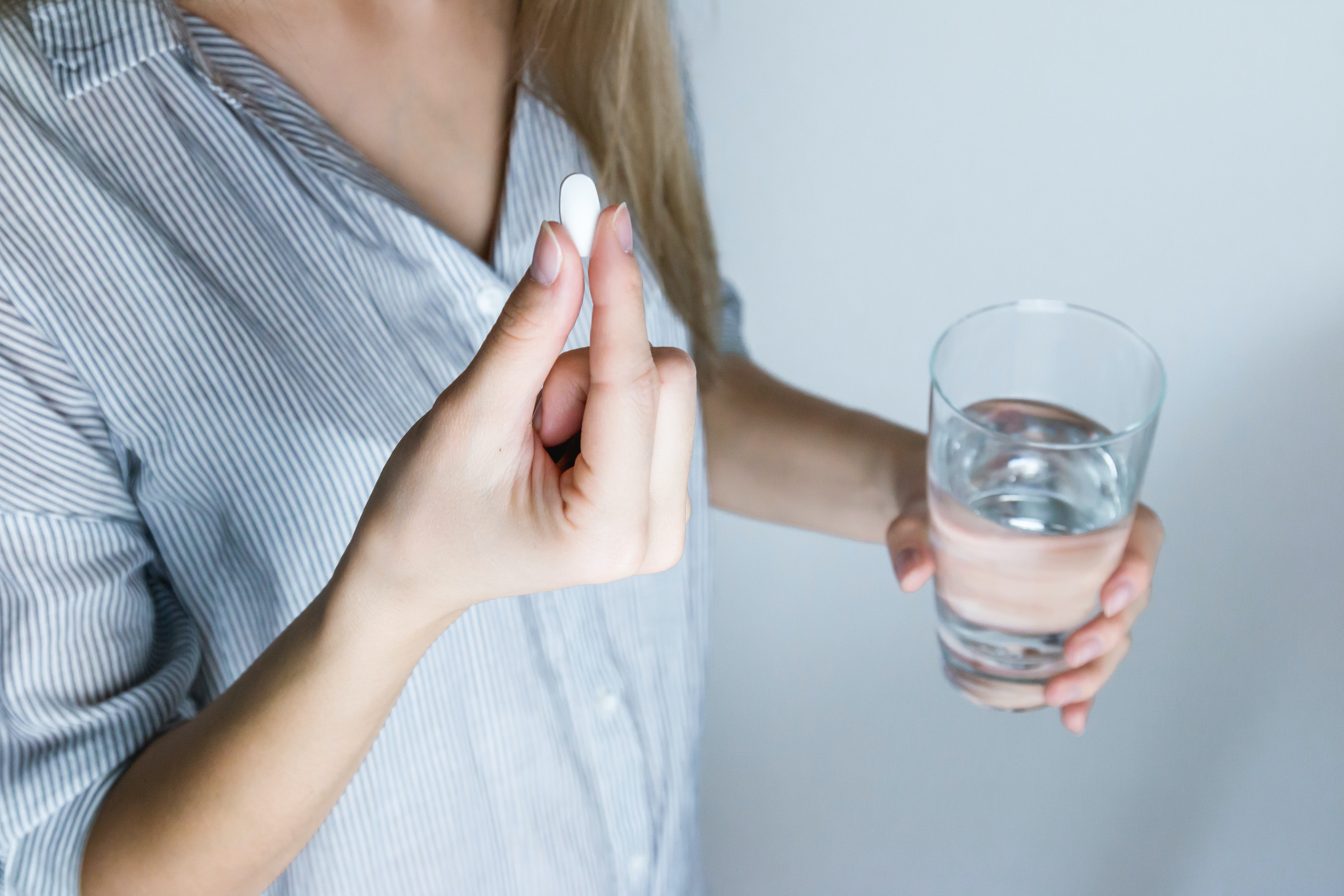 Mujer sosteniendo una pastilla y un vaso con agua. | Foto: Pexels