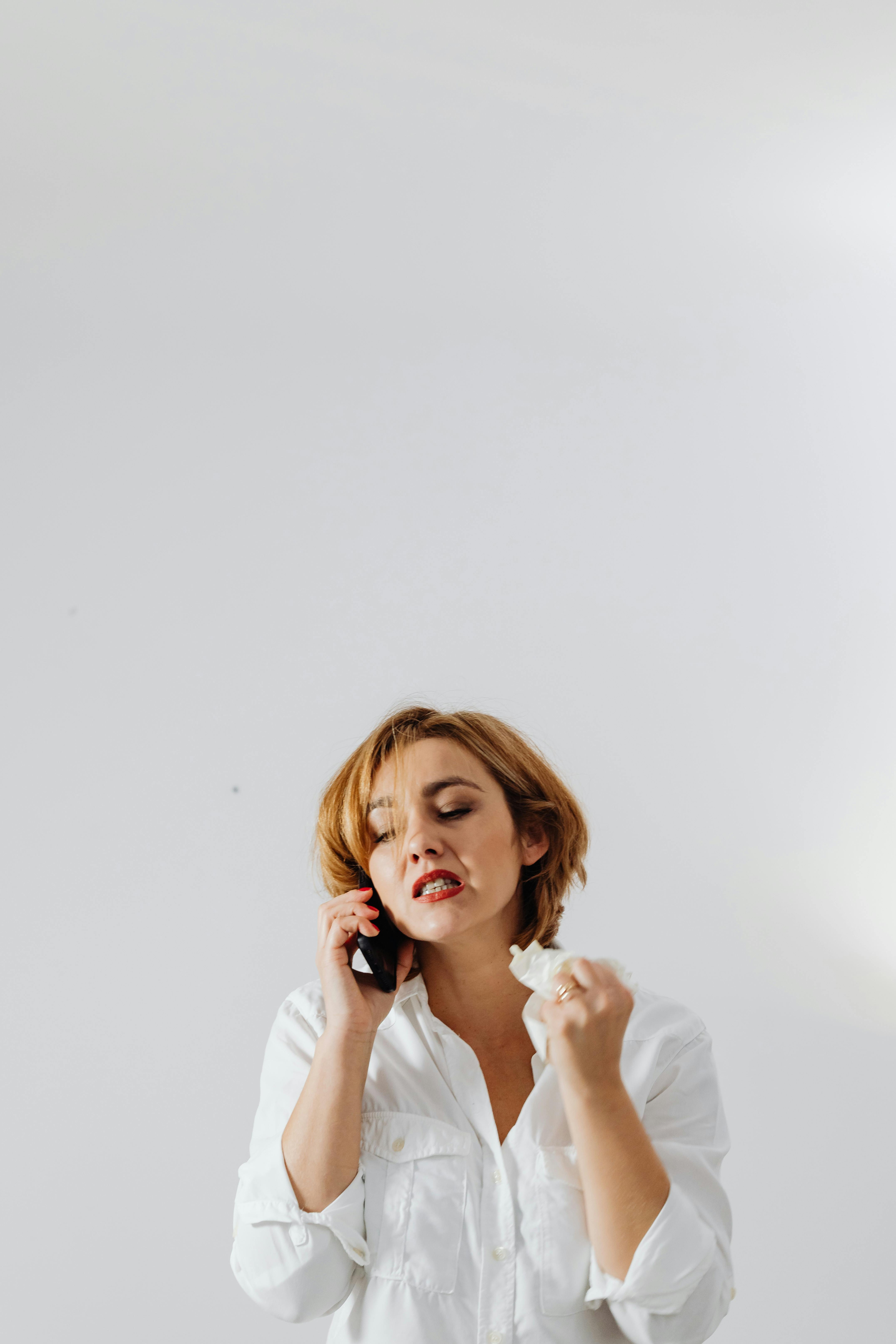 Una mujer disgustada y enfadada sostiene un pañuelo de papel mientras habla por teléfono | Foto: Pexels
