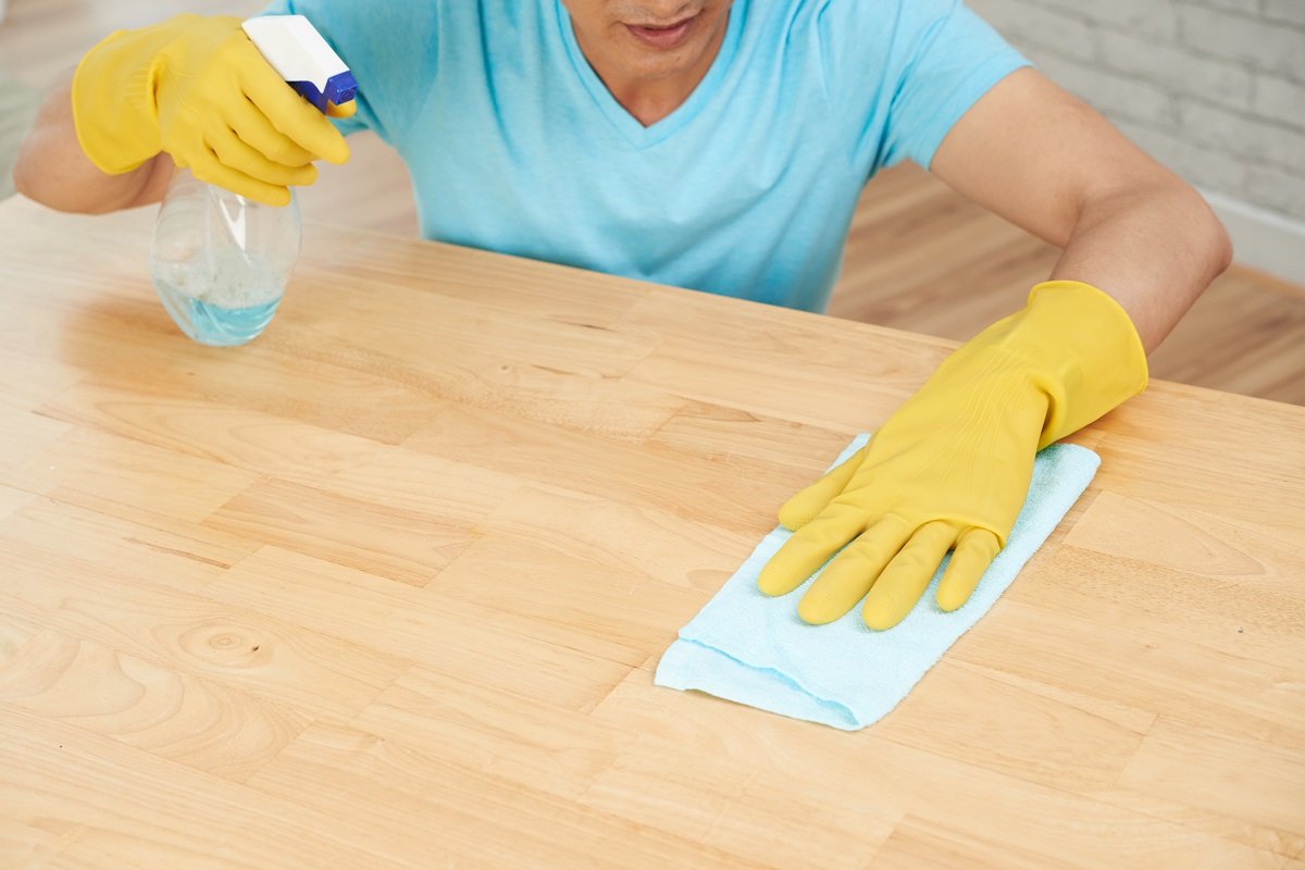Hombre con guantes de goma desinfecta una superficie con rociador y tela. | Foto: Freepik