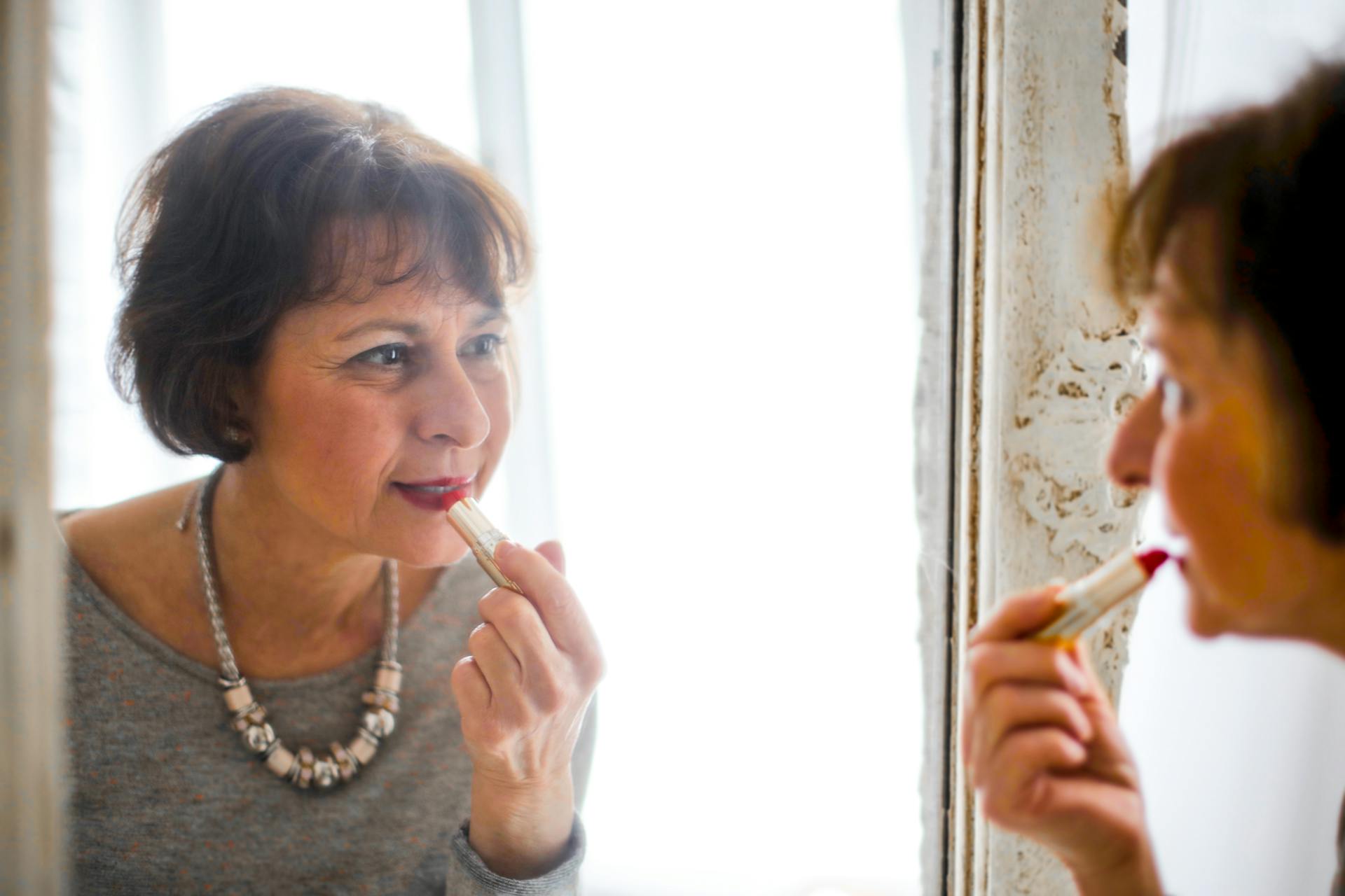 Una mujer mayor pintándose los labios | Foto: Pexels