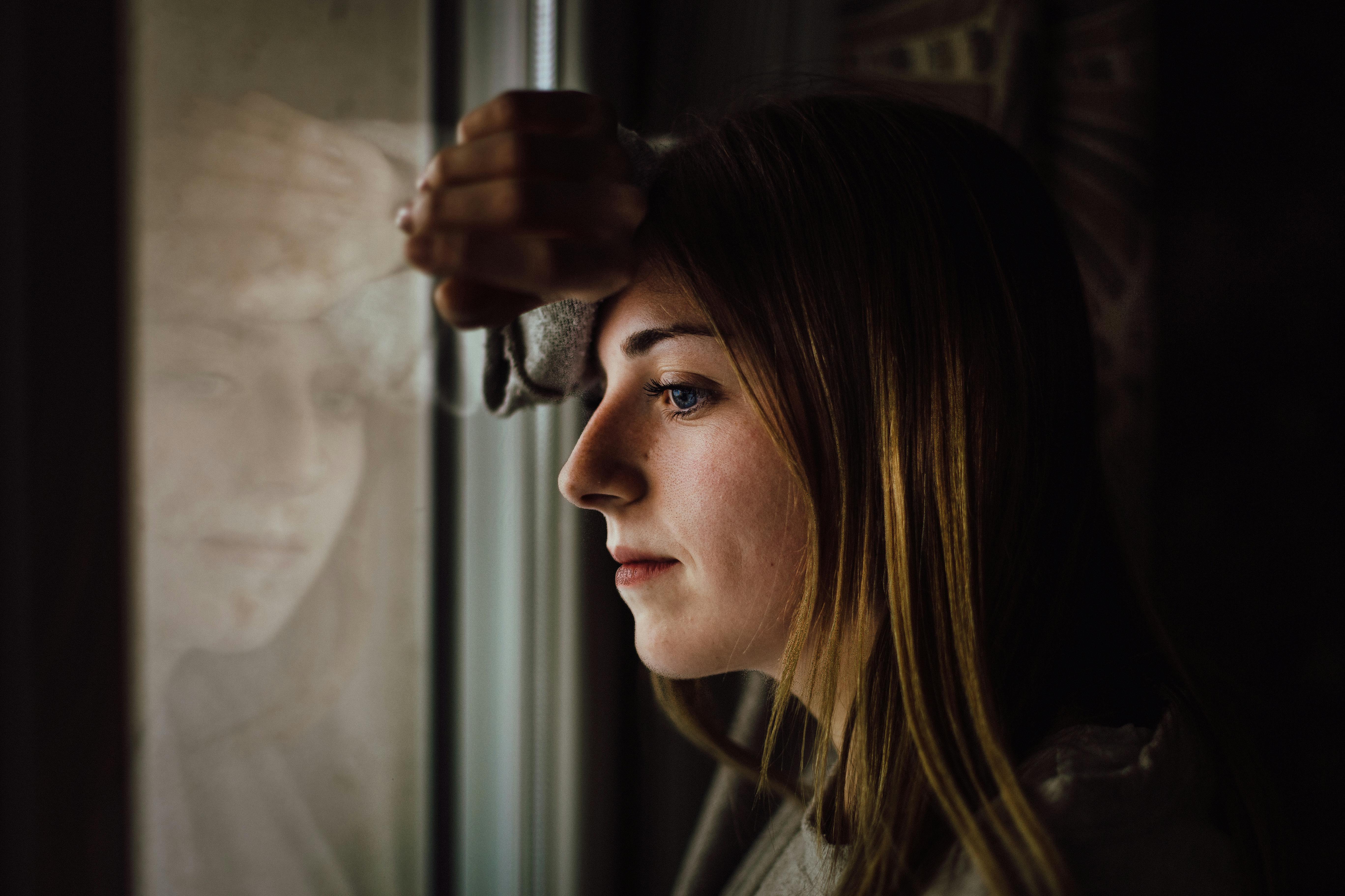 Una mujer mirando por la ventana y ensimismada | Fuente: Pexels