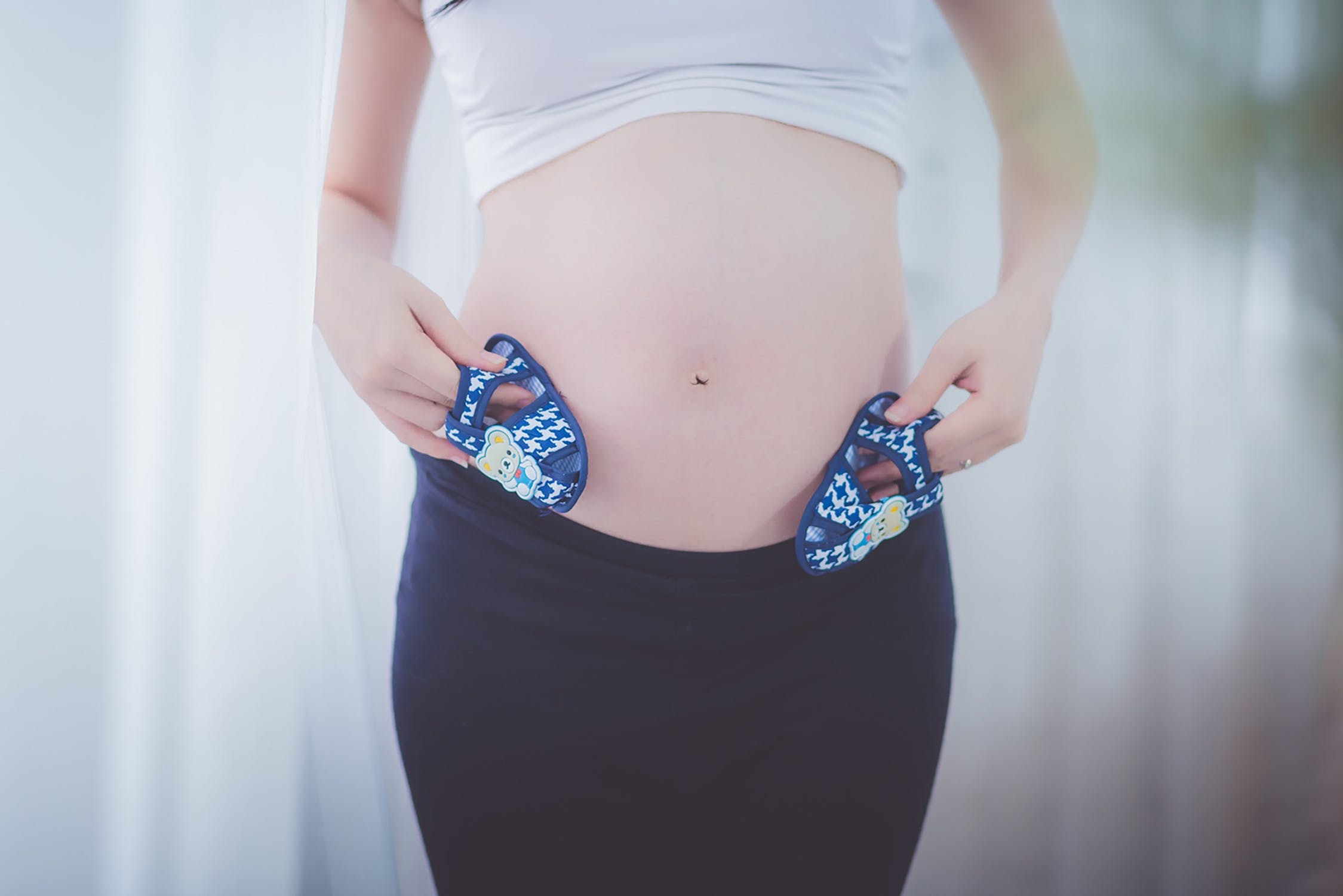 Mujer embarazada mostrando su vientre abultado con pequeños zapatos en sus manos. | Imagen: Pexels