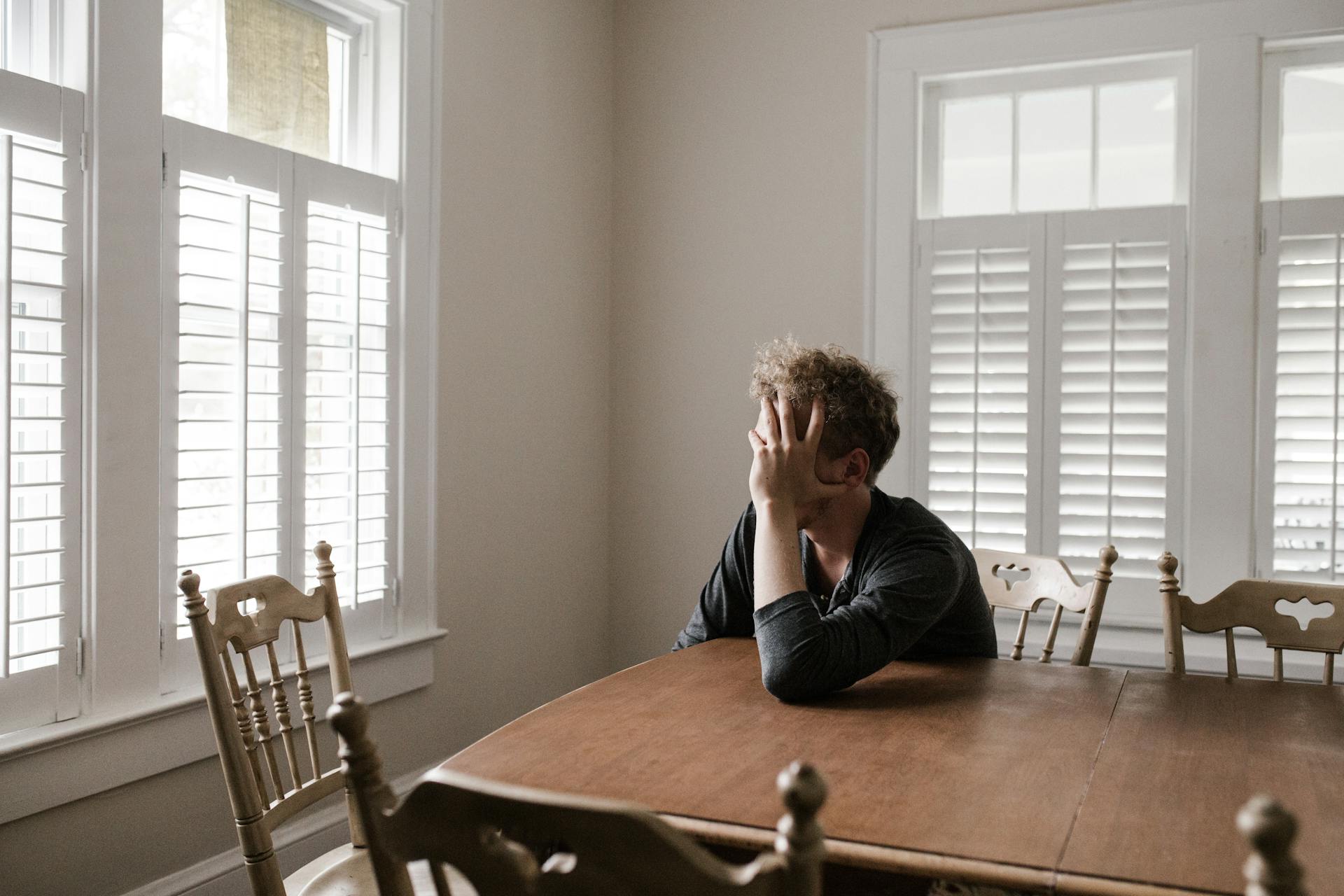 Un hombre alterado apoyado en una mesa de madera | Fuente: Pexels