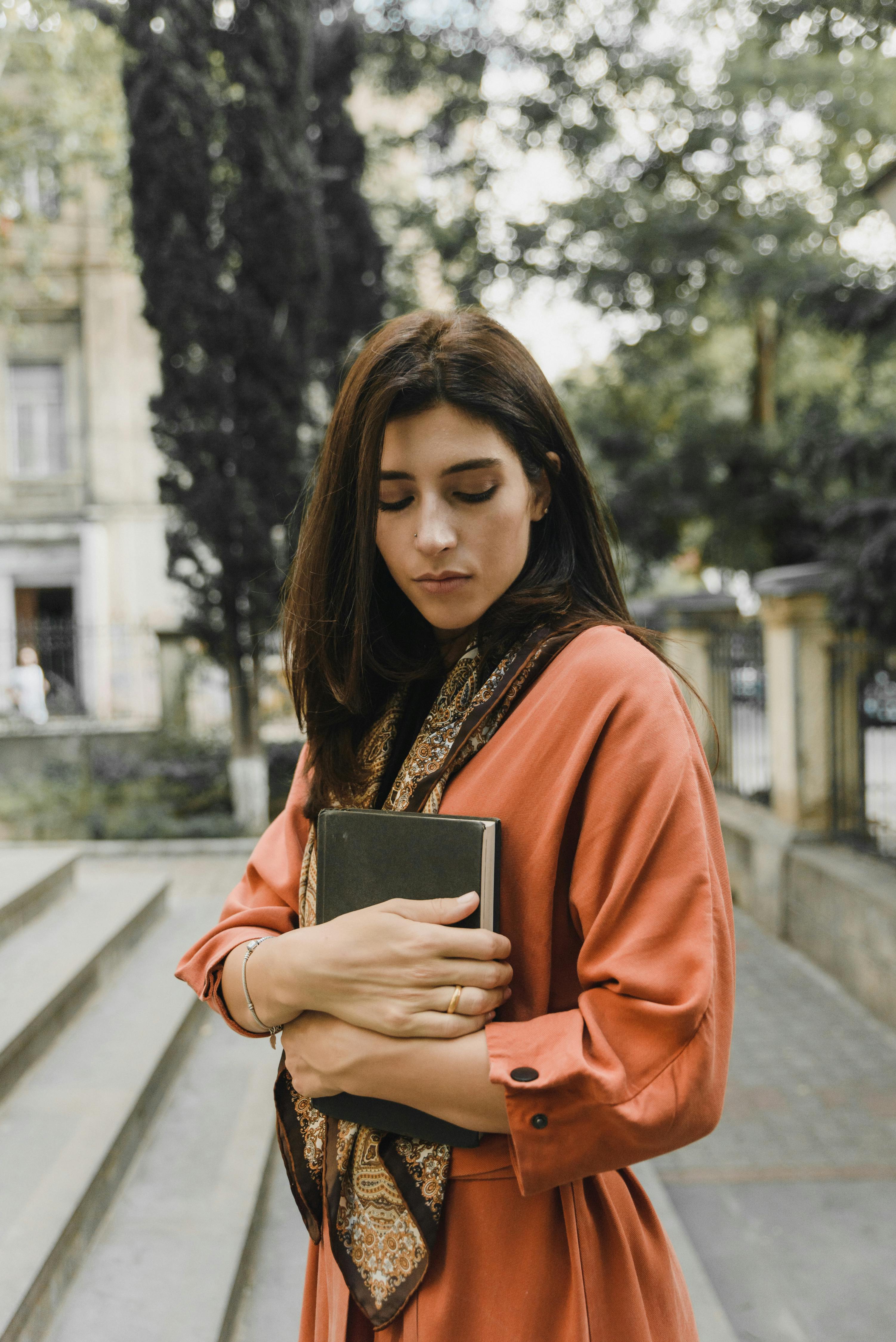 Una mujer triste mirando hacia abajo mientras sostiene un libro | Fuente: Pexels