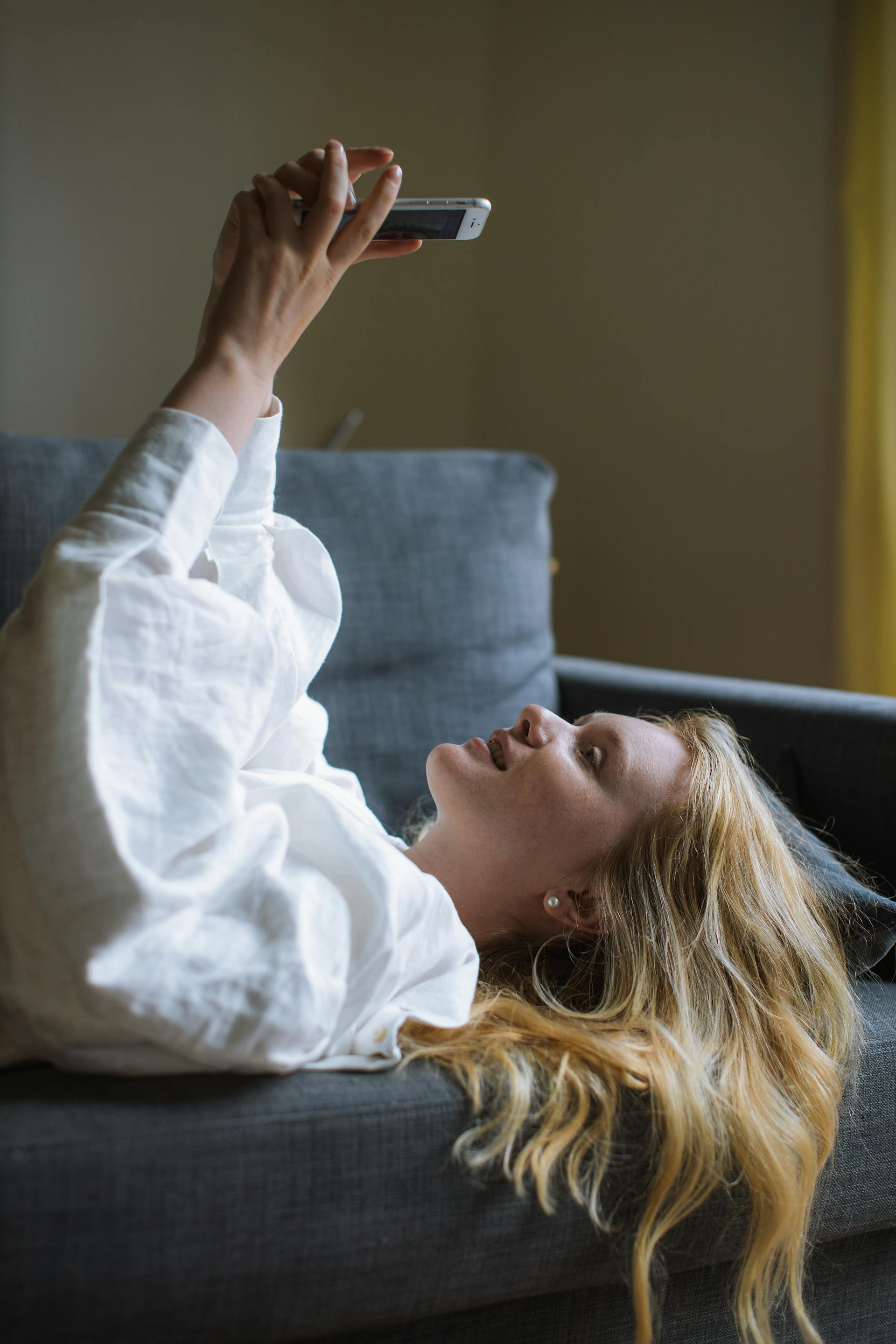 Una joven utilizando su teléfono mientras está tumbada en un sofá | Fuente: Pexels