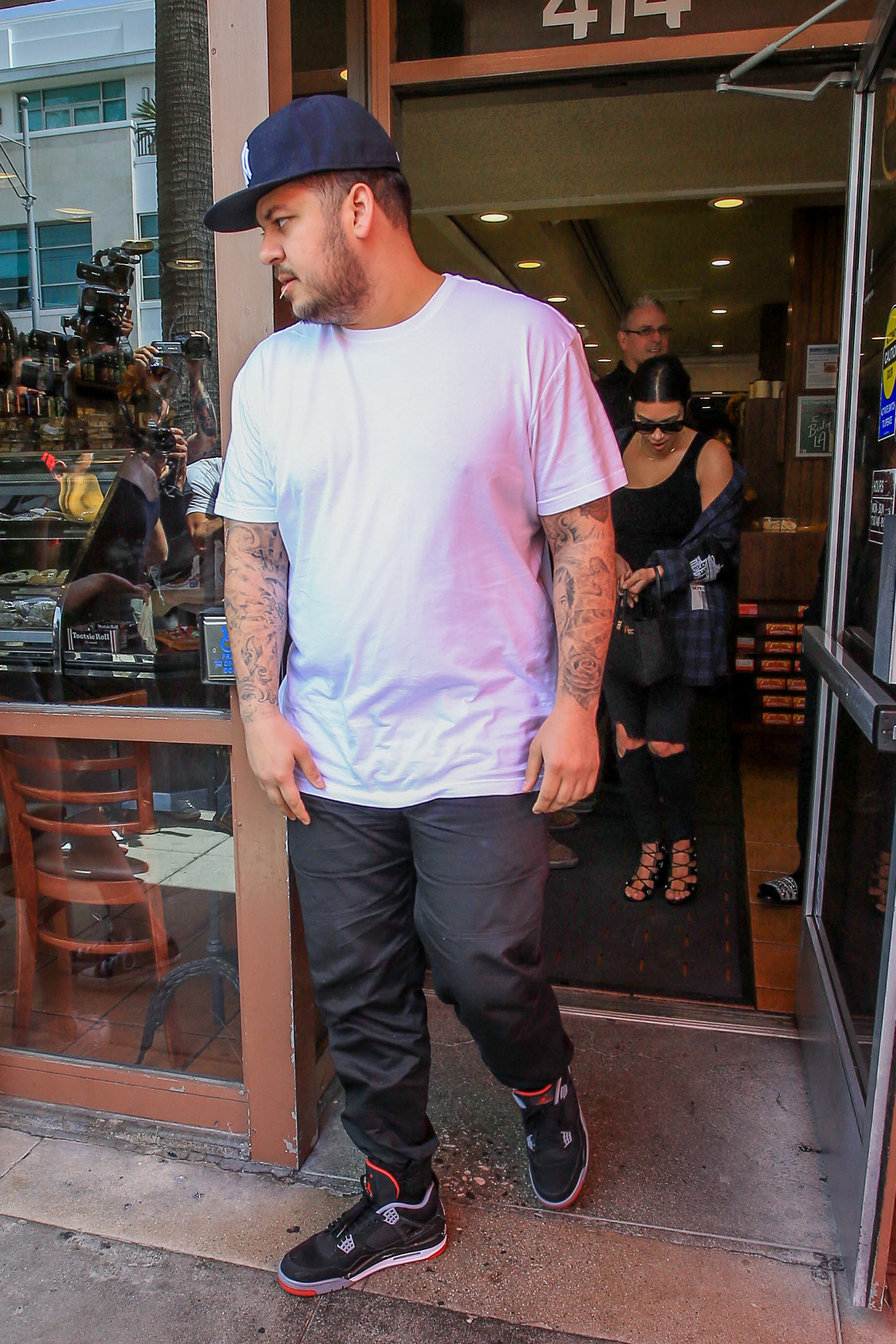 Rob Kardashian sale de un restaurante de Los Ángeles con una camiseta blanca y una gorra de béisbol, seguido de cerca por Kim Kardashian. La foto recoge una de sus pocas salidas públicas con su hermana en una época en la que poco a poco se iba sintiendo más cómodo apareciendo en público. | Fuente: Getty Images.
