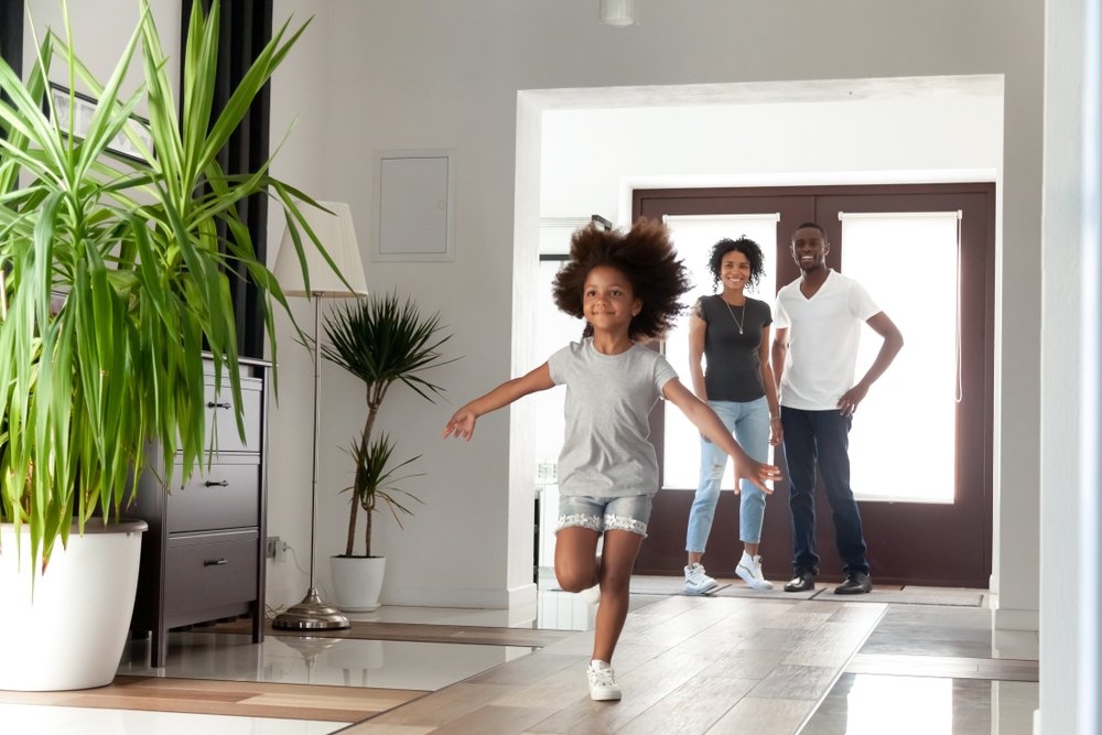 Niña emocionada corre en la casa mientras la observan sus padres. | Foto: Shutterstock