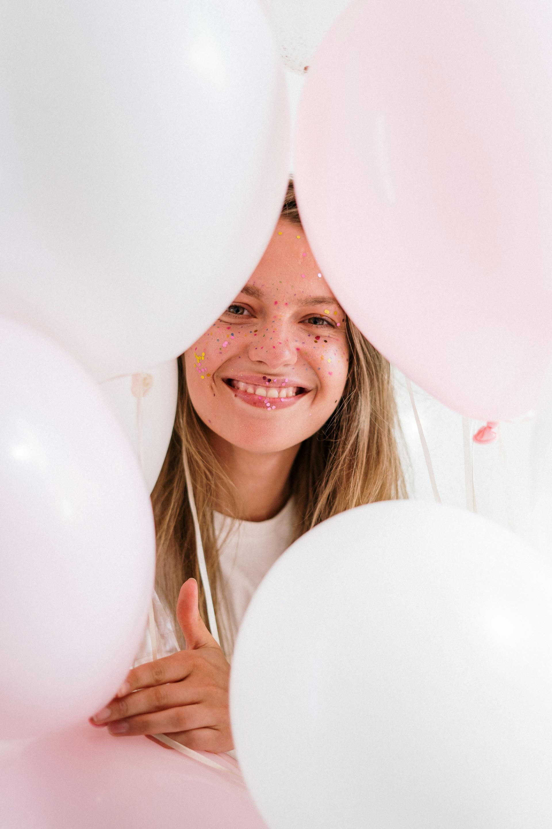 Una joven sonriente sujetando globos rosas y blancos | Fuente: Pexels