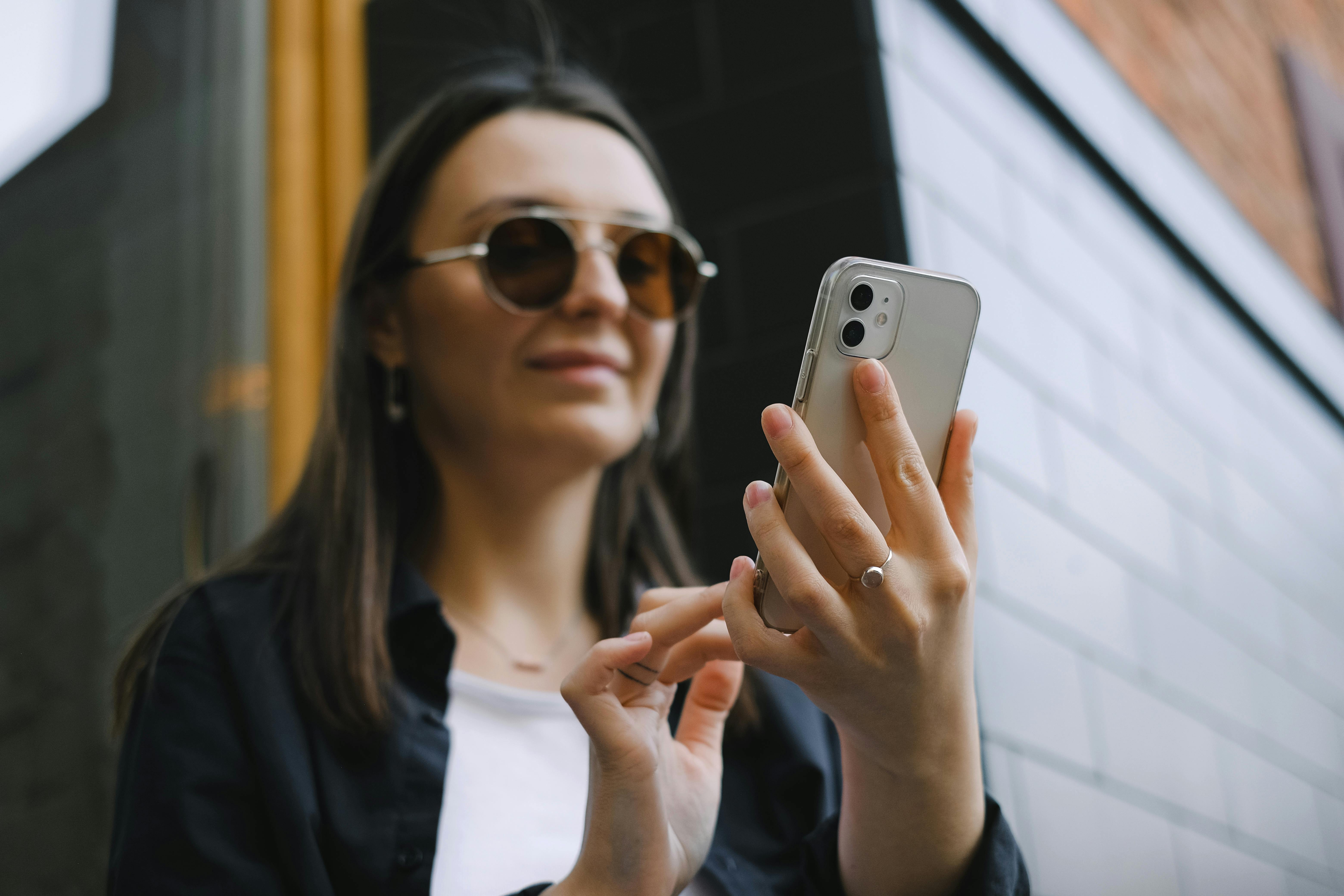 Una mujer sonriente tecleando en su teléfono | Fuente: Pexels