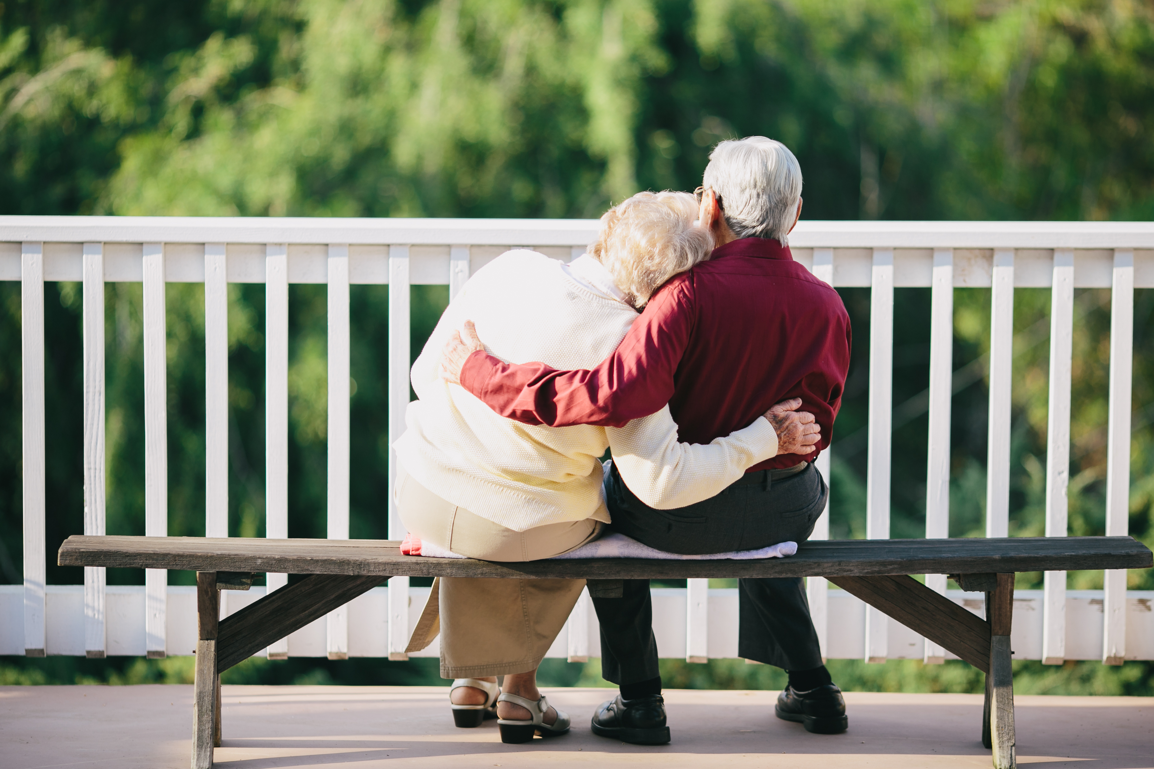 Una pareja de ancianos se abraza sentada en un banco al aire libre | Fuente: Shutterstock