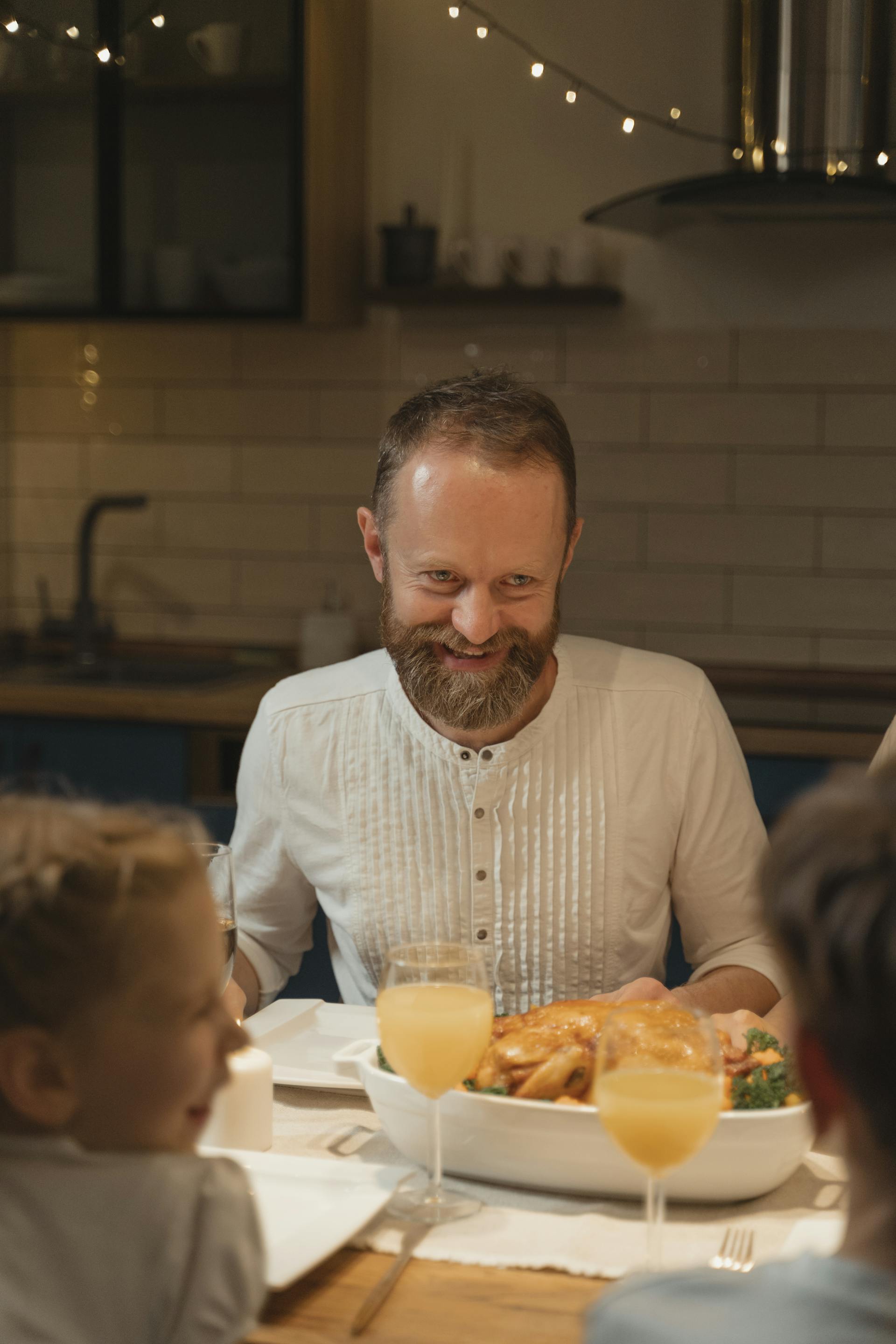 Un hombre con barba sonríe sentado a la mesa | Fuente: Pexels