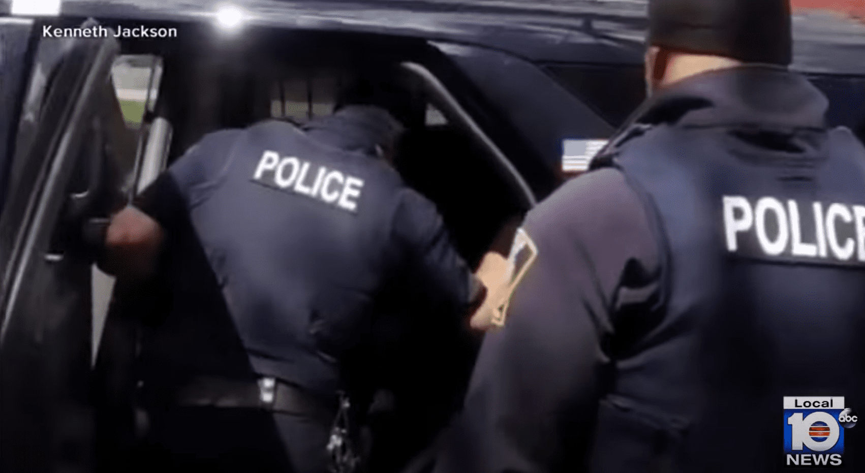 Los policías fotografiados tratando de meter al niño en la patrulla. | Foto: Youtube.com/WPLG Local 10