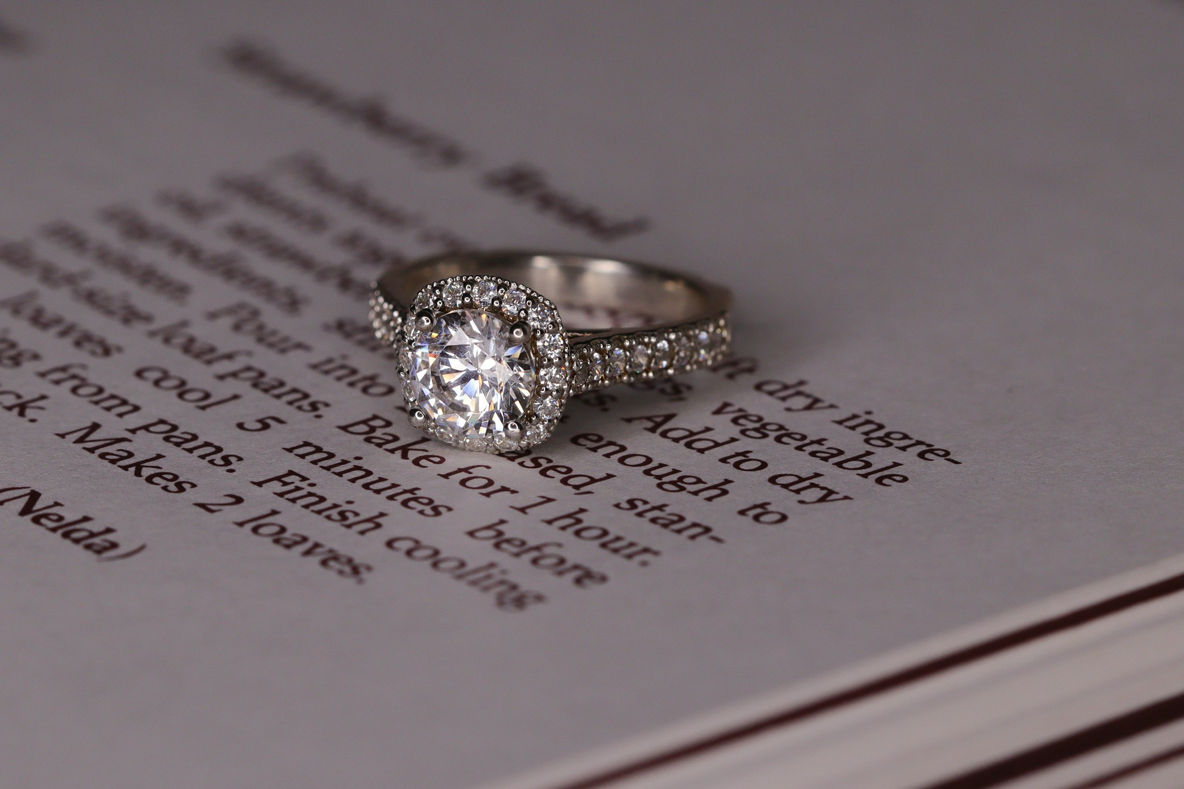 Un anillo de compromiso de diamantes estilo halo de oro blanco sobre un libro | Fuente: Unsplash