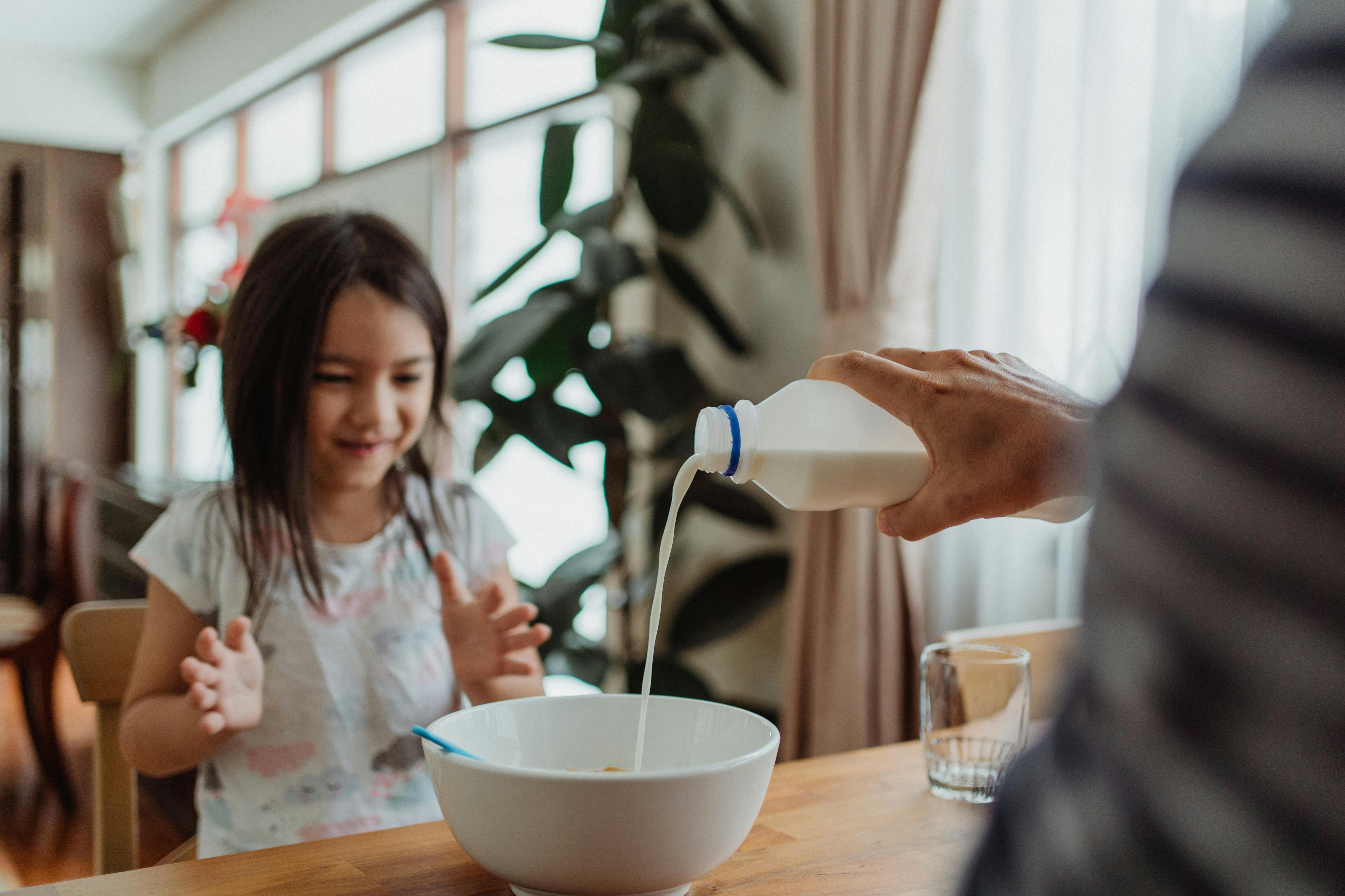 Un hombre vierte leche en un cuenco para una niña en la mesa del desayuno | Fuente: Pexels