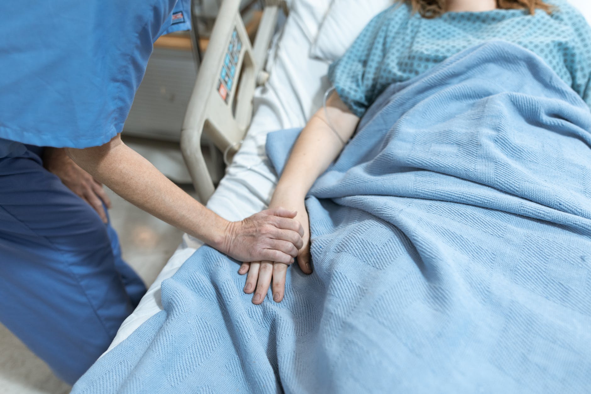 Una persona acostada en una cama clínica mientras alguien le toma la mano. | Foto: Pexels