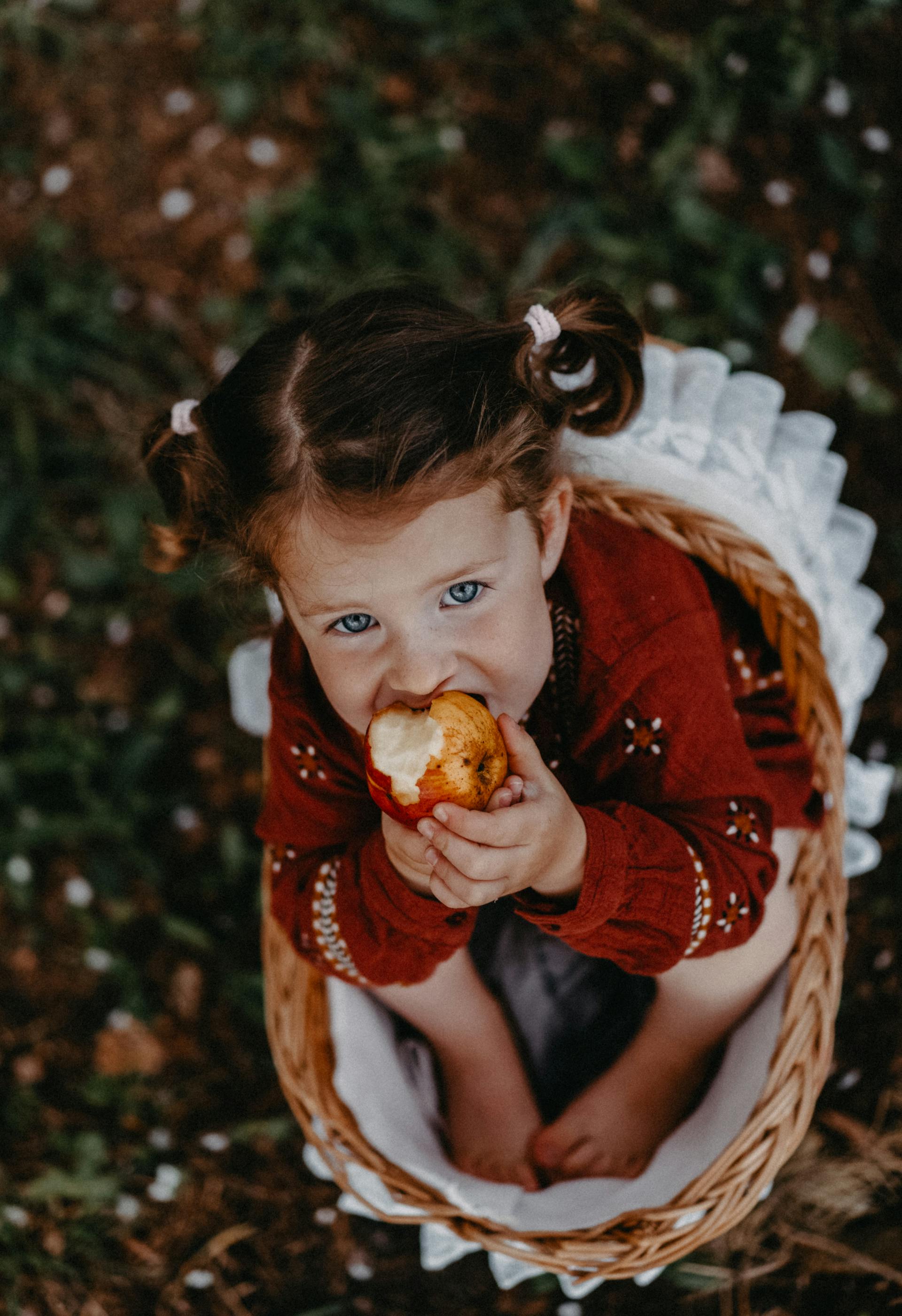 Una niña sentada en una cesta comiendo una manzana | Fuente: Pexels