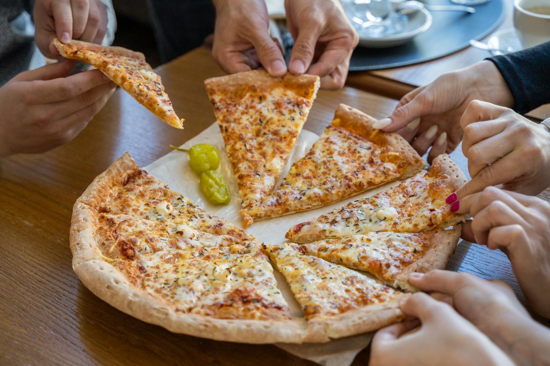 Gente tomando porciones de una pizza | Fuente: Pexels