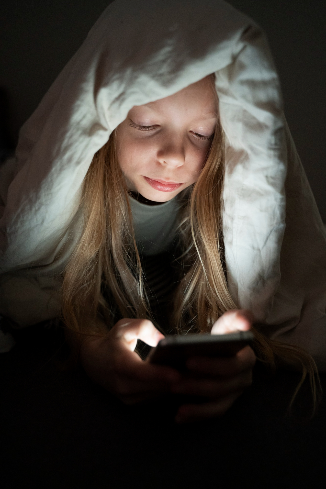 Niña cubierta con una manta usa su teléfono | Foto: Freepik