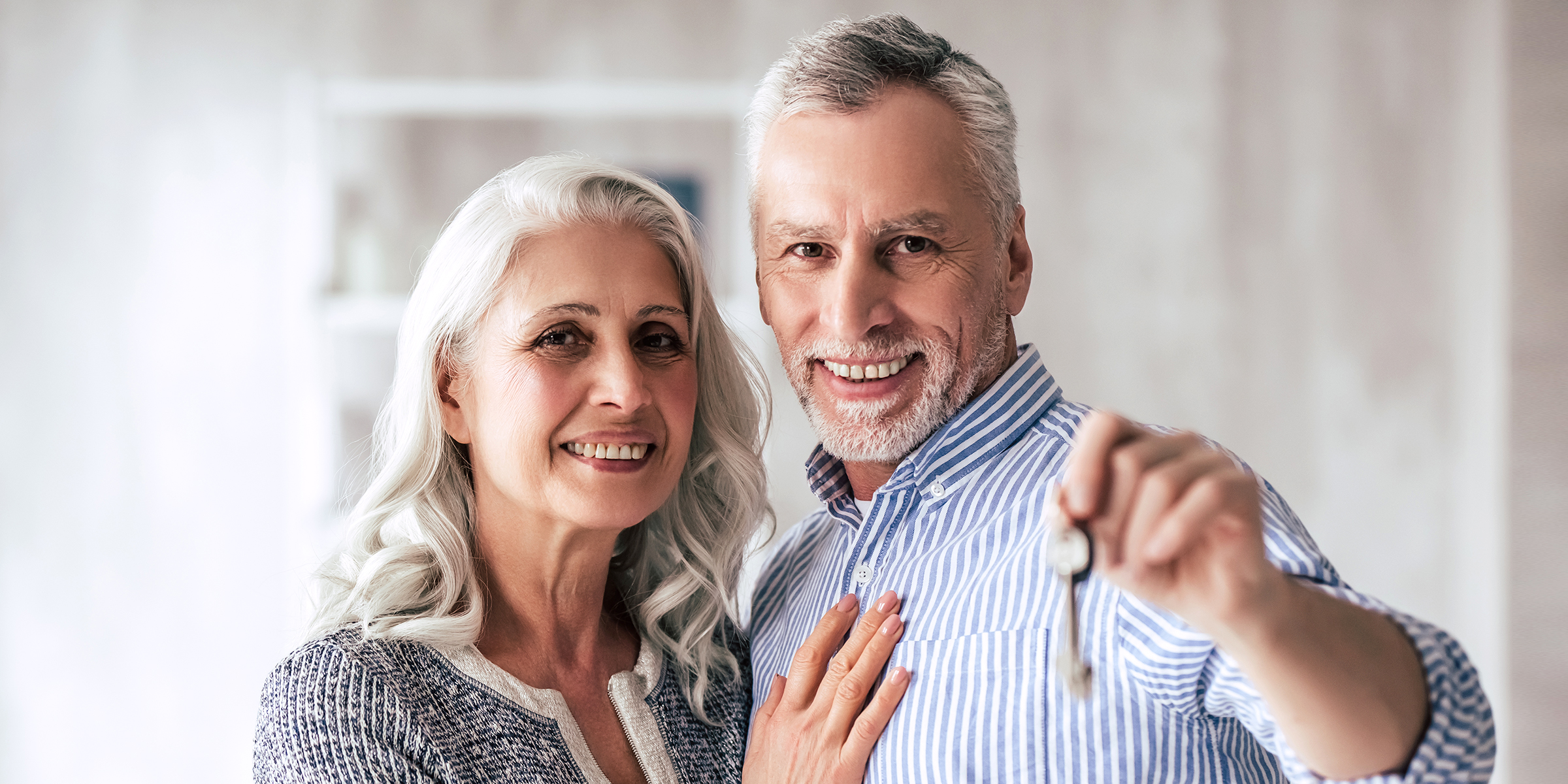 Feliz pareja de ancianos sonriendo con una llave de casa en la mano | Fuente: Shutterstock