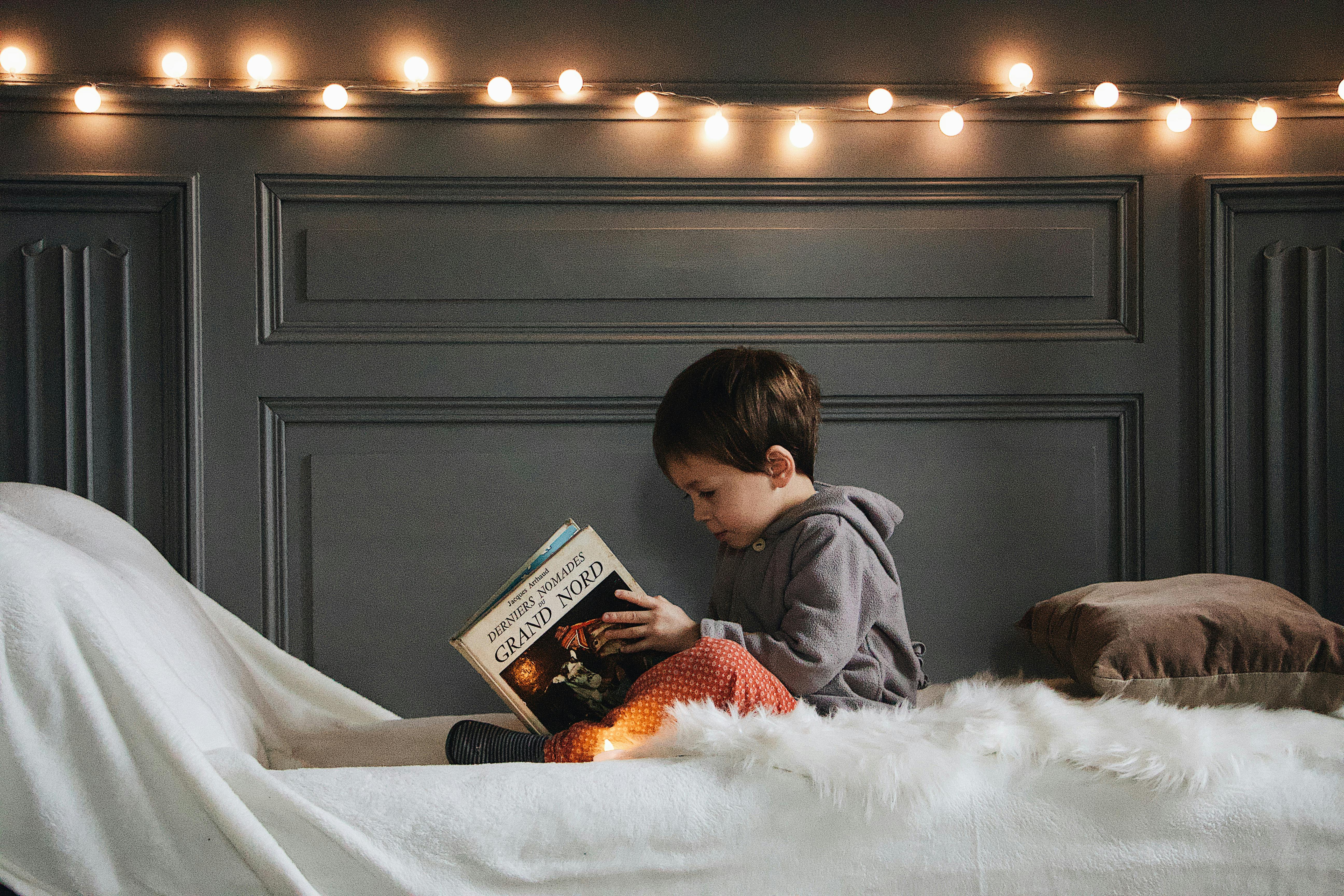 Un niño pequeño leyendo un libro en la cama | Fuente: Pexels