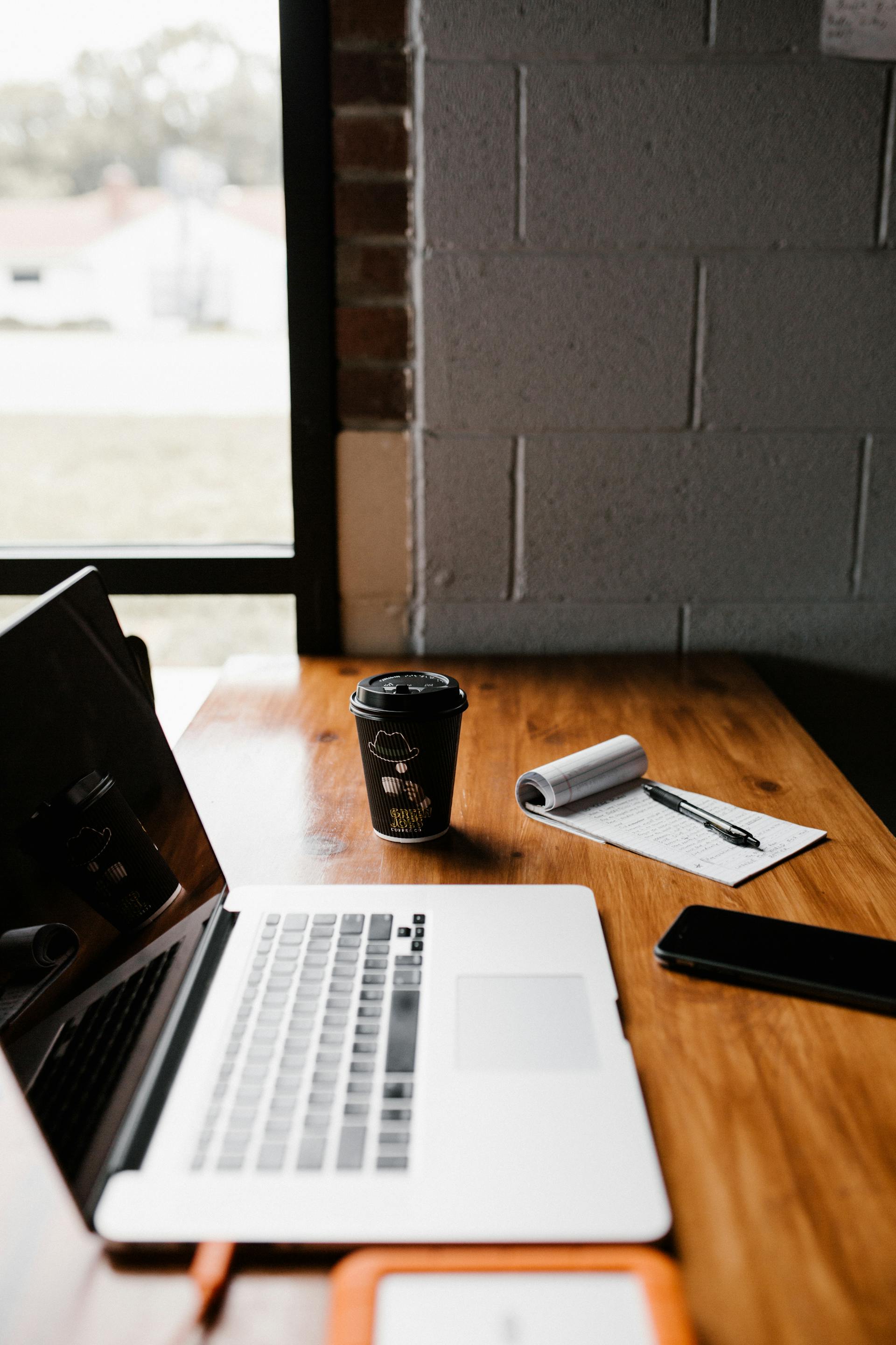 Un vaso de café para llevar junto a un portátil en un escritorio | Fuente: Pexels