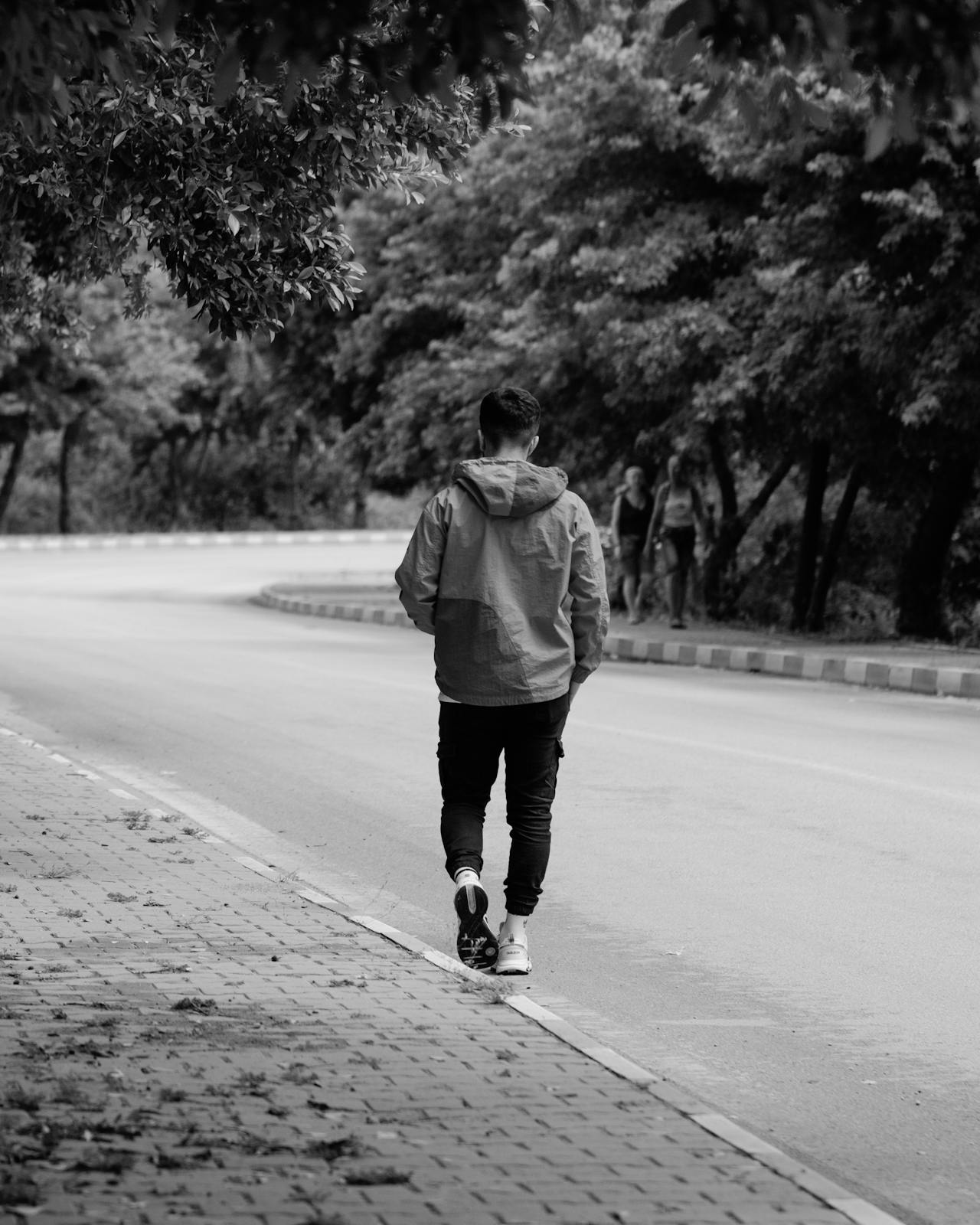 Toma en escala de grises de un joven caminando por la carretera | Fuente: Pexels