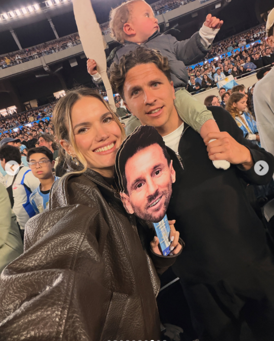 Eva Bargiela compartió una cálida selfie familiar en medio de la multitud celebrando la noche de despedida de Messi. La modelo sonrió con una campera de cuero marrón junto a su esposo, quien cargaba en andas a su hijo Faustino, mientras sostenían frente a ellos la careta con la cara del capitán argentino. | Fuente: Instagram/evabargiela