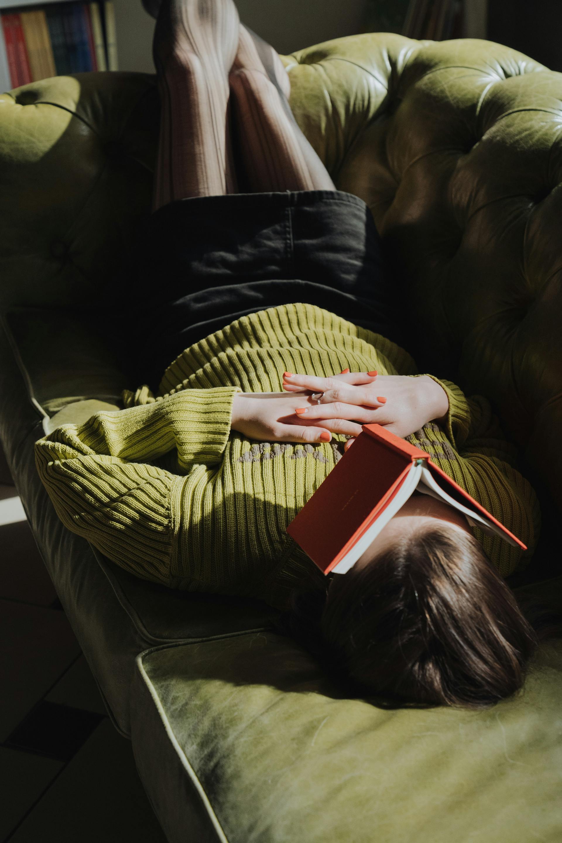 Una mujer tumbada en un sofá con un libro | Fuente: Pexels
