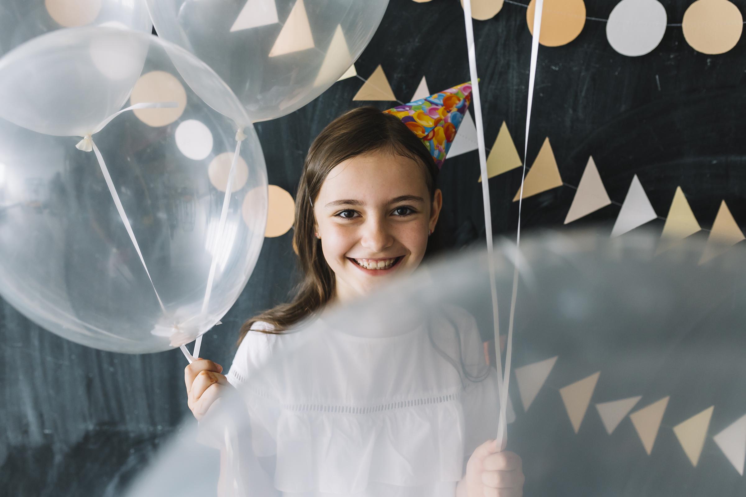 Niña sonriente sujetando globos | Fuente: Freepik