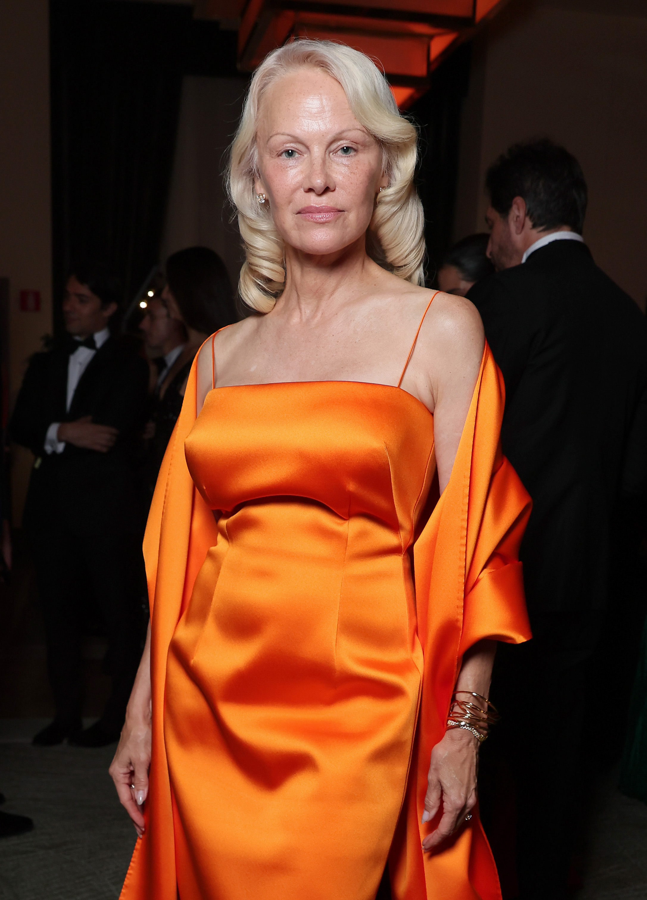 Pamela Anderson combinó sus característicos rizos rubios platino con un llamativo vestido de satén naranja, demostrando que su estilo hollywoodiense ha evolucionado mucho más allá de la glamurosa imagen de «Los vigilantes de la playa» de los años 90. | Fuente: Getty Images
