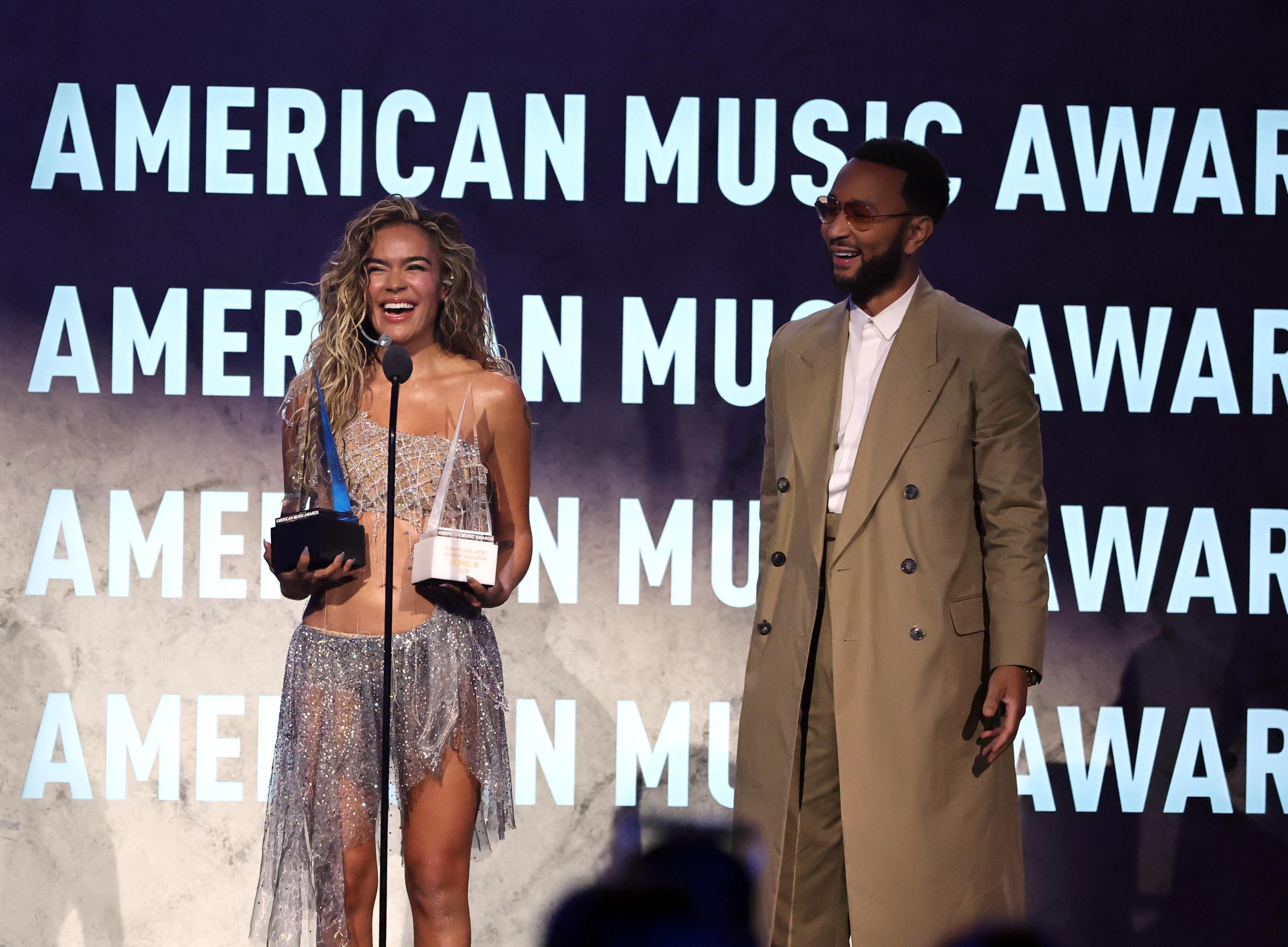 Karol G recibe el premio International Artist Award of Excellence de manos de John Legend en el escenario durante la 52ª edición de los American Music Awards en el MGM Grand Garden Arena el 25 de mayo de 2026 en Las Vegas, Nevada. | Fuente: Getty Images
