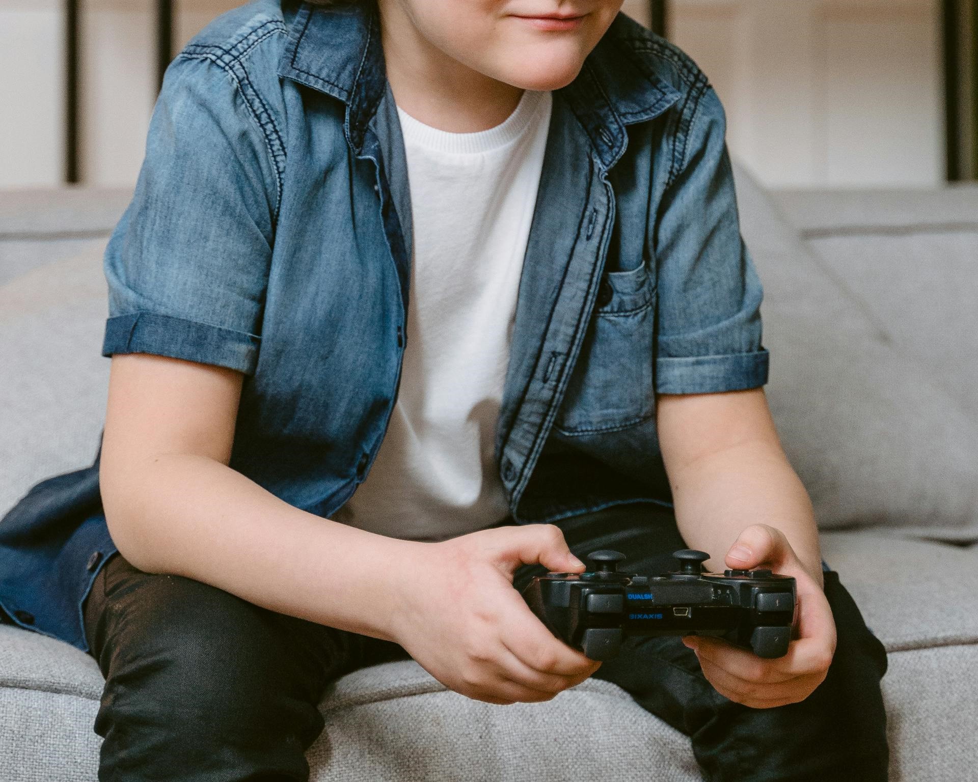 Un niño sentado en el sofá y sujetando una consola de juegos | Fuente: Pexels