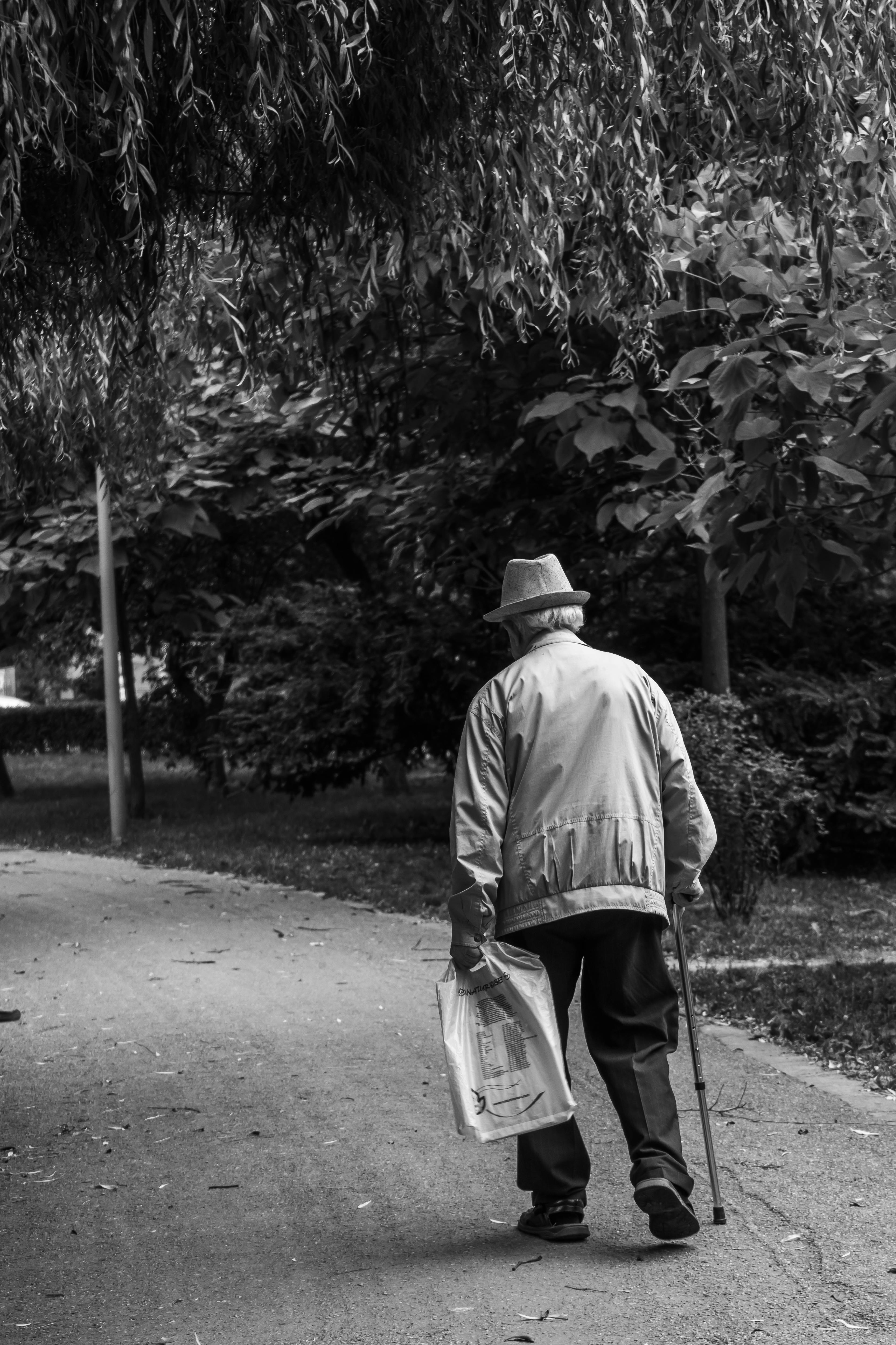 Escala de grises de un anciano caminando con un bastón y un periódico | Fuente: Pexels