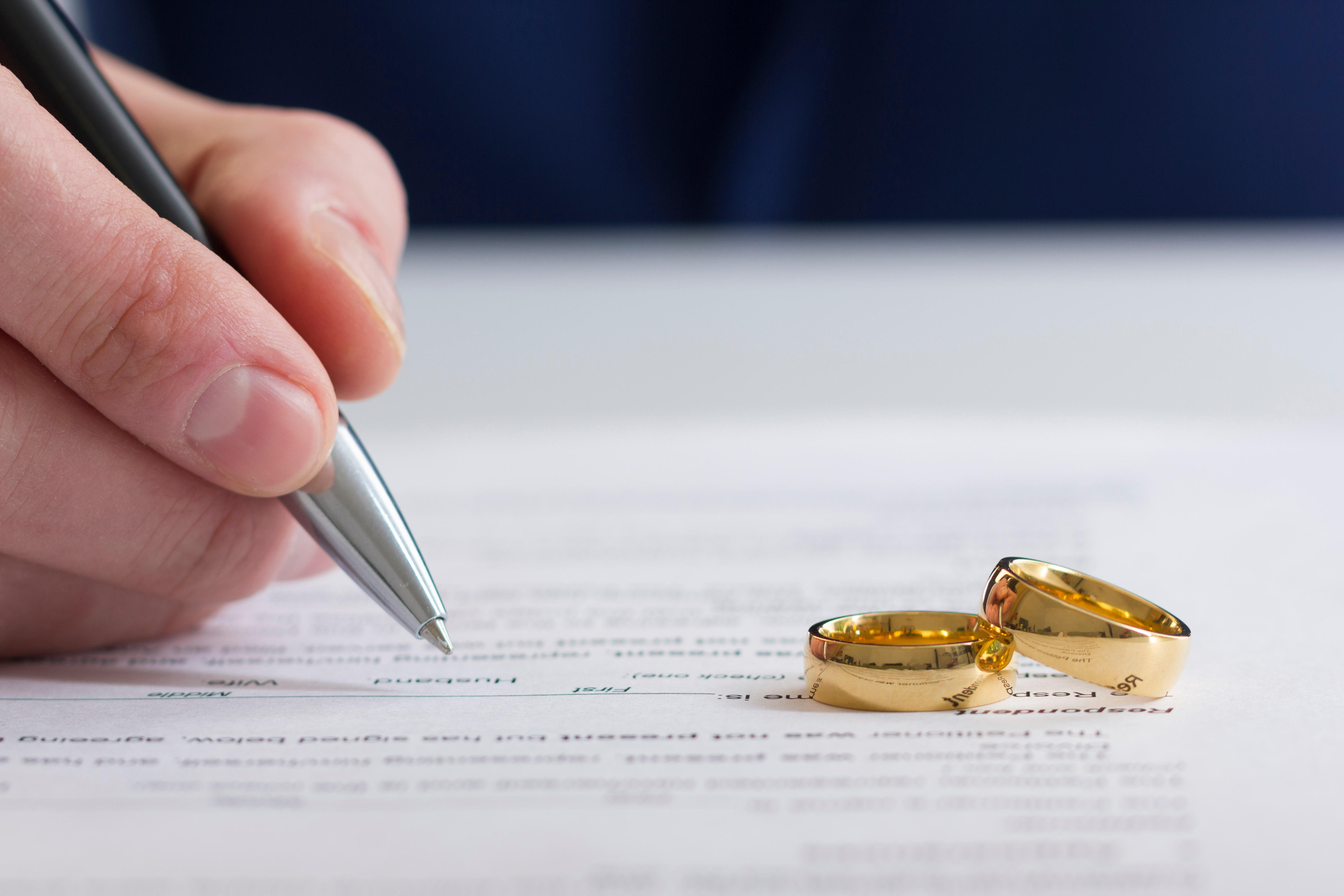 Una persona firmando papeles de divorcio con dos anillos encima | Foto: Shutterstock