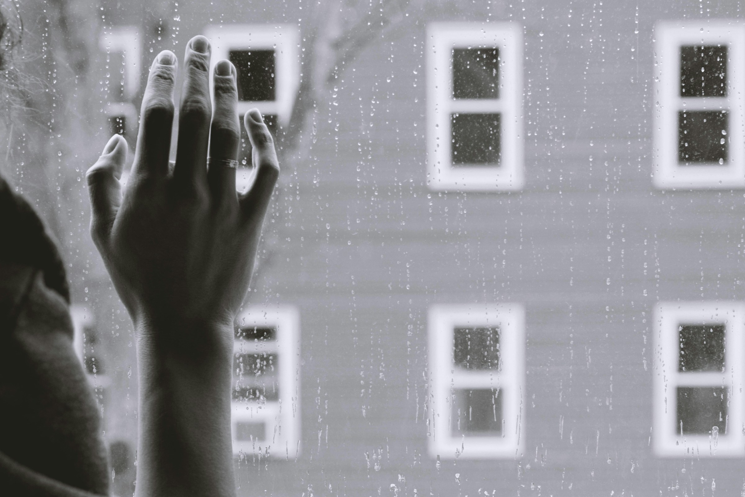 Foto en escala de grises de la mano derecha de una mujer sobre un cristal | Foto: Pexels